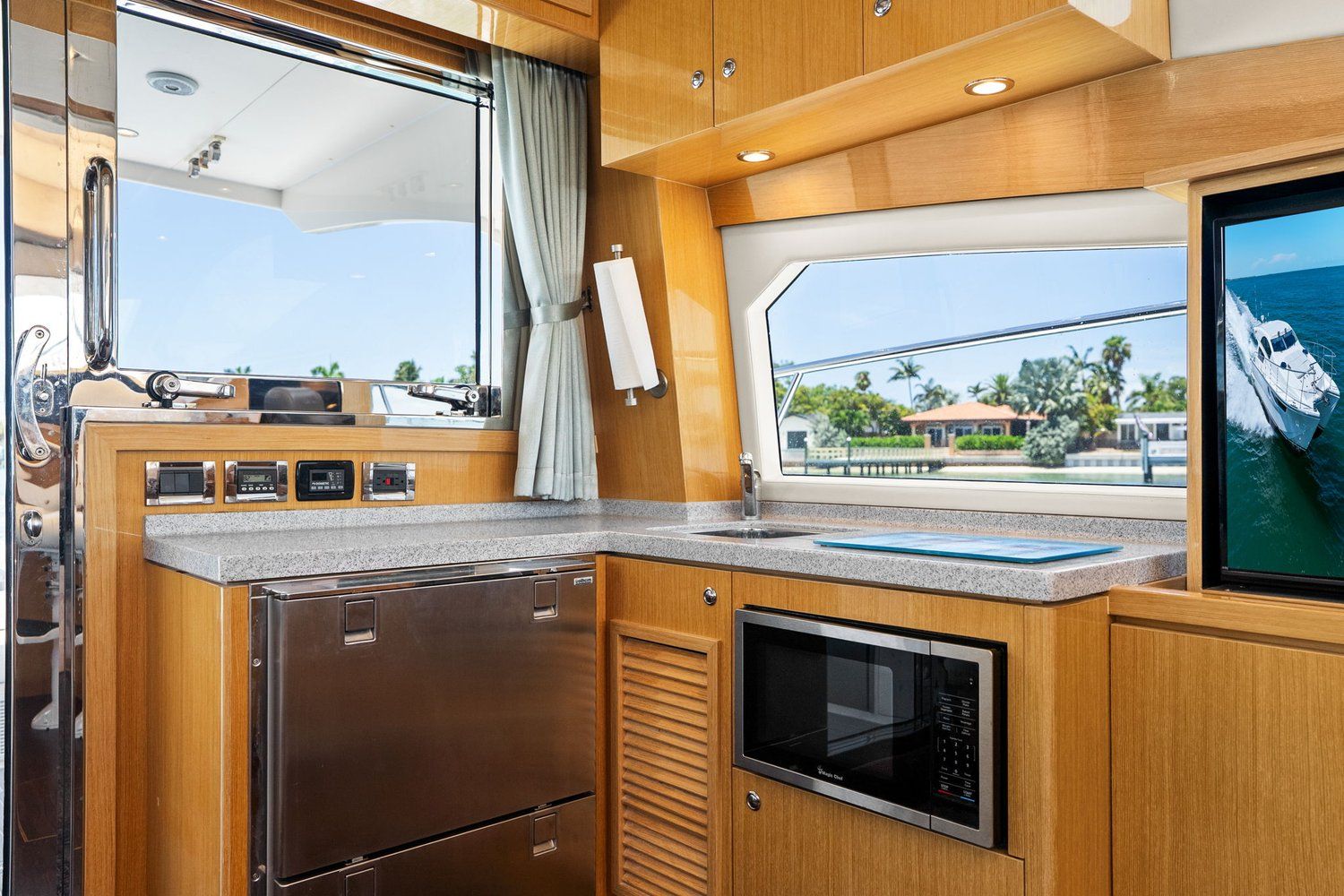 Interior of a modern yacht kitchen with wooden cabinets, microwave, and large window overlooking the water.