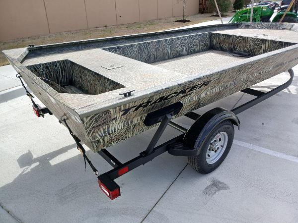2025 Tracker GRIZZLY 1860 Utility boat on trailer, camouflage design, parked outdoors.