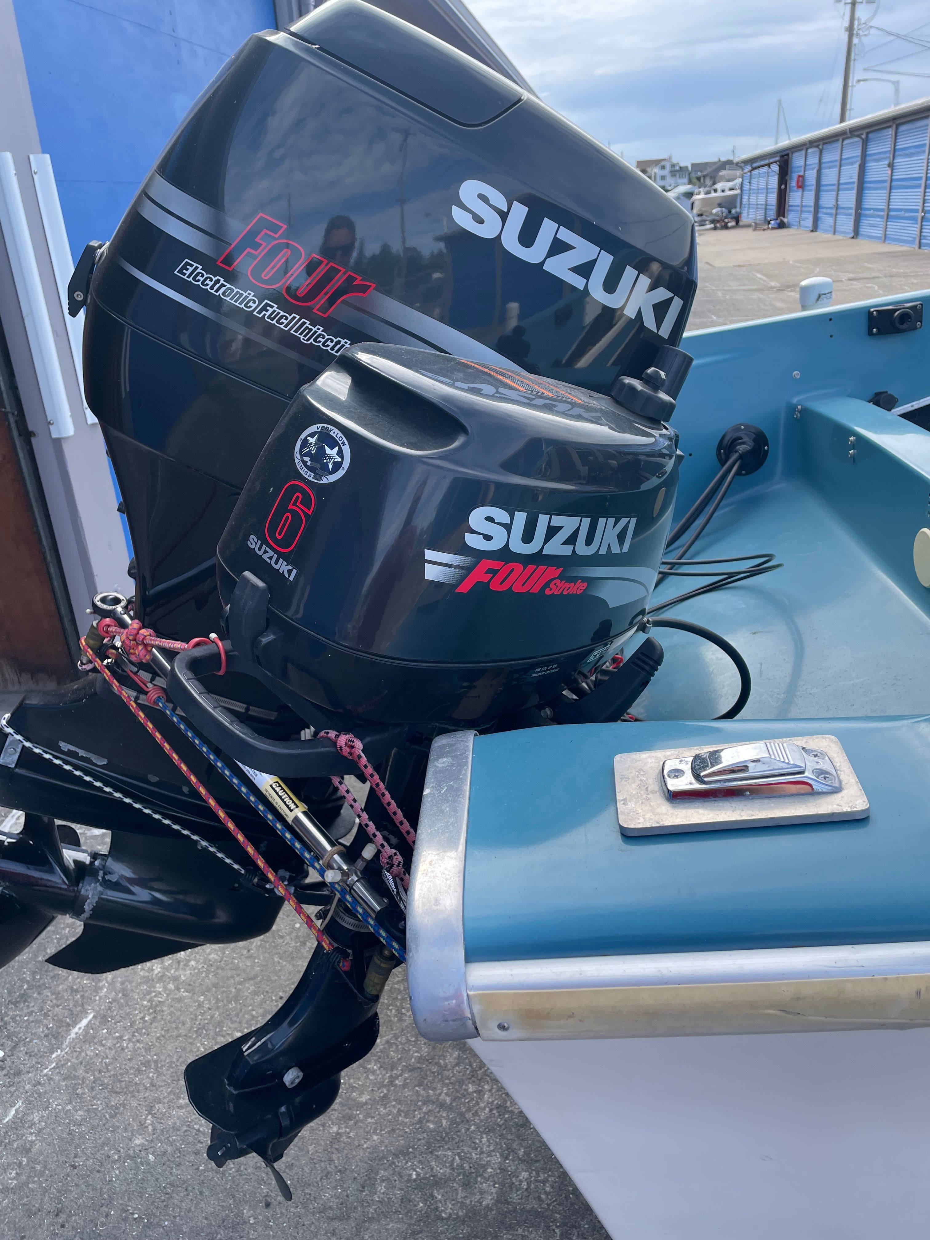 Outboard motors on a boat, including a Suzuki engine, in a harbor setting.