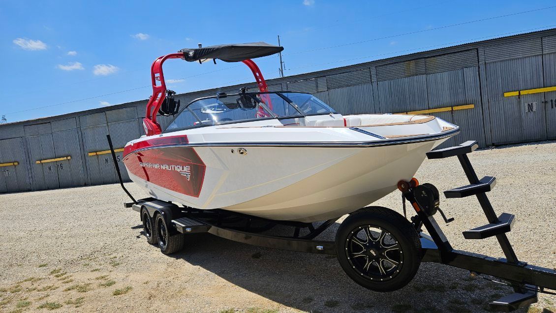 A 2018 Super Air Nautique G23 on a trailer in front of a storage building.