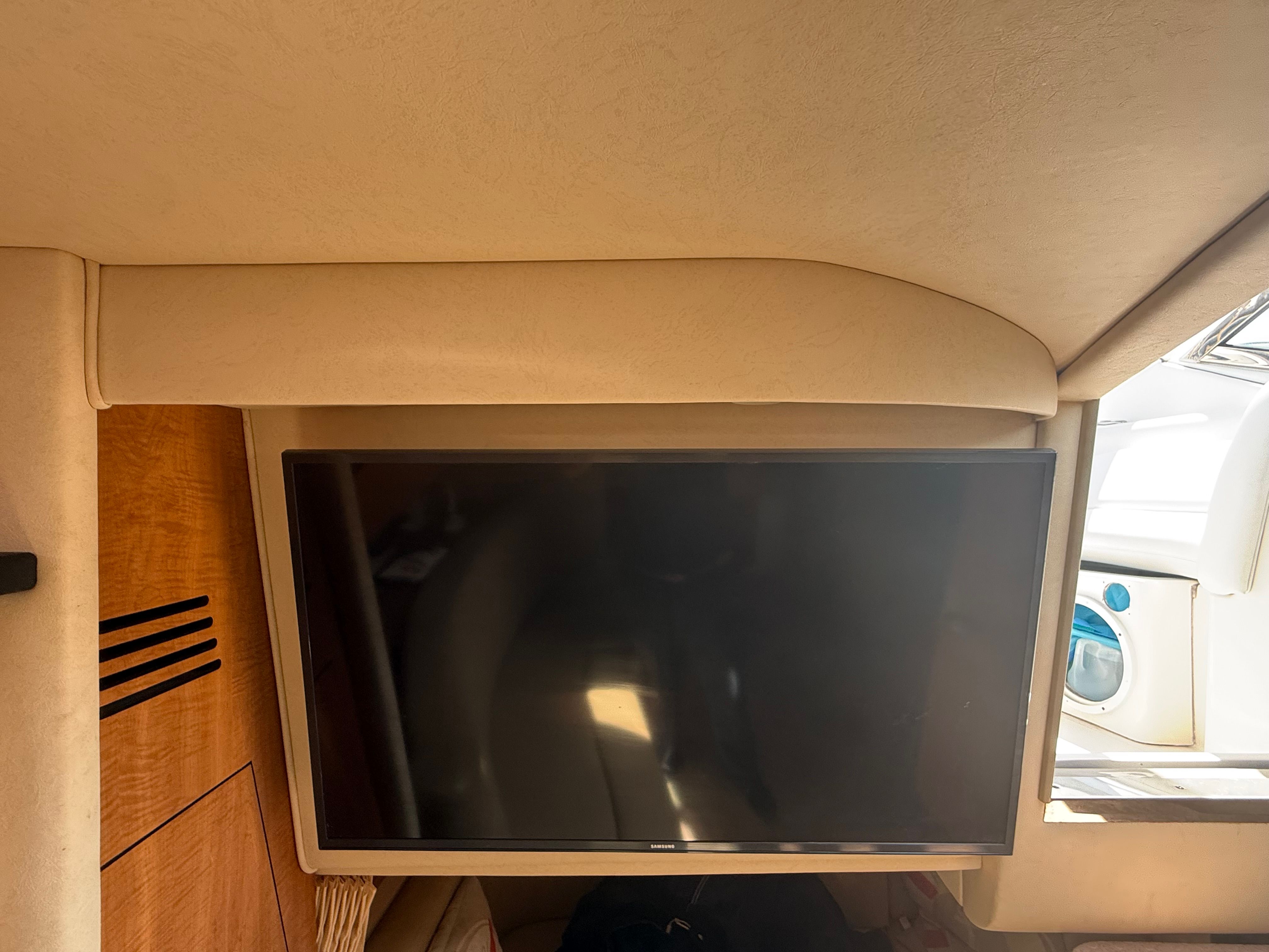 Interior of a Sea Ray Sundancer 320 with a large flat-screen TV mounted on the wall.