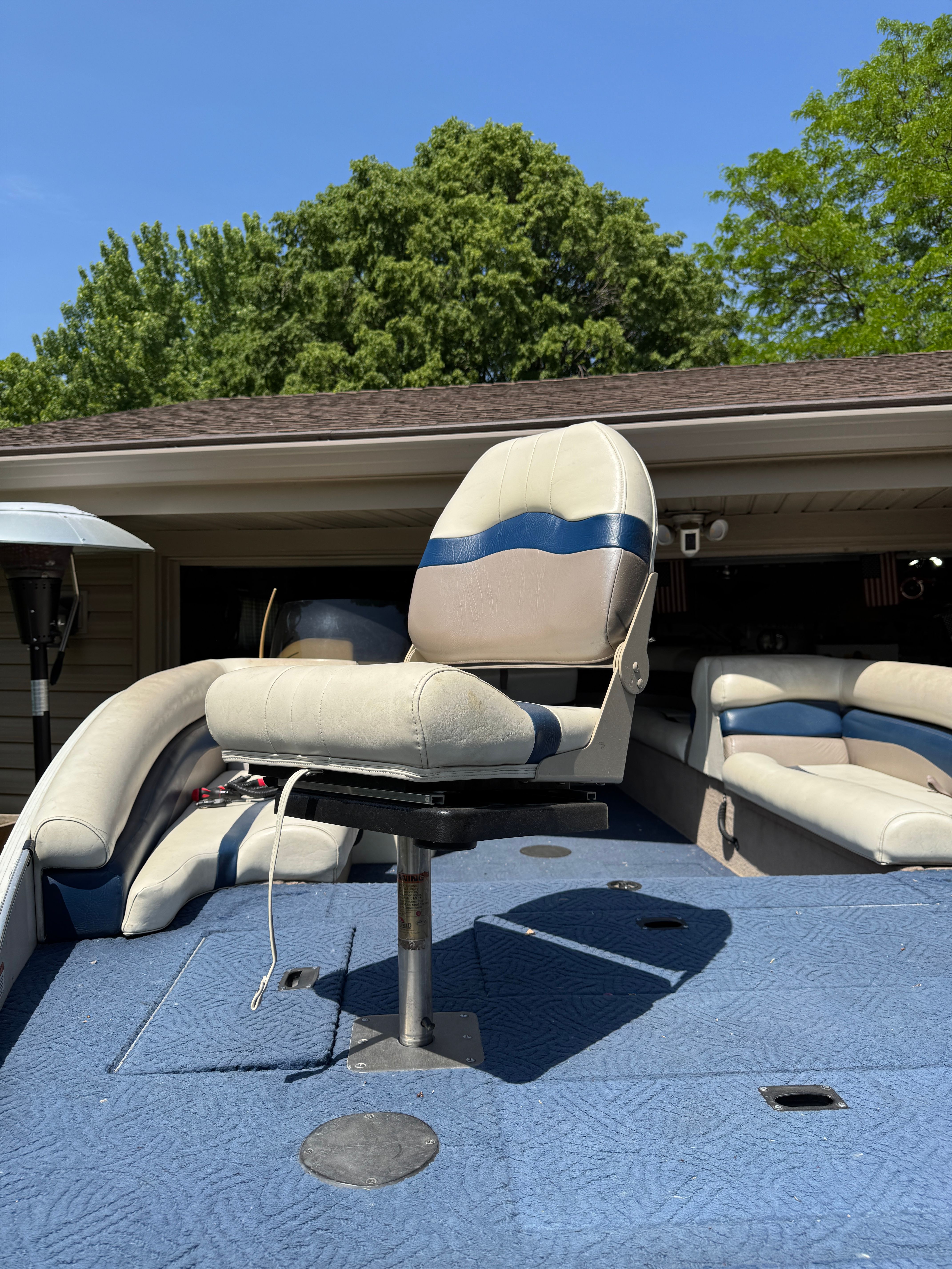 A boat with blue and white seats on a blue carpeted deck, surrounded by trees.