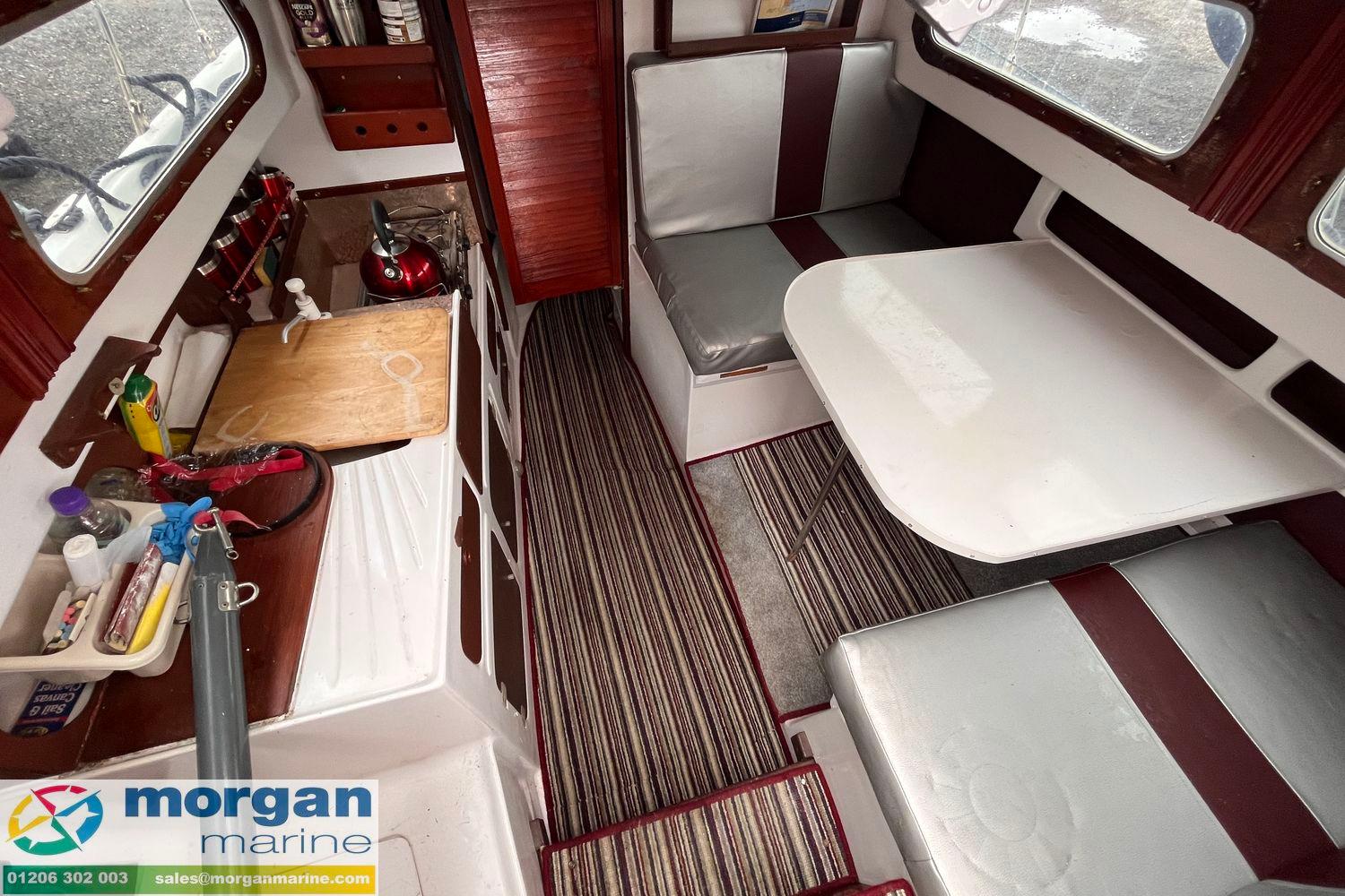 1979 Leisure 23 boat interior with kitchenette, dining area, and striped carpet flooring.