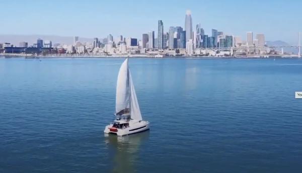 Sailboat Bali 4.8 (2021) cruising near a city skyline on a clear day.