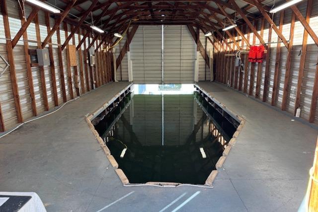 1960 custom boathouse interior with water dock, wooden beams, and open garage door.