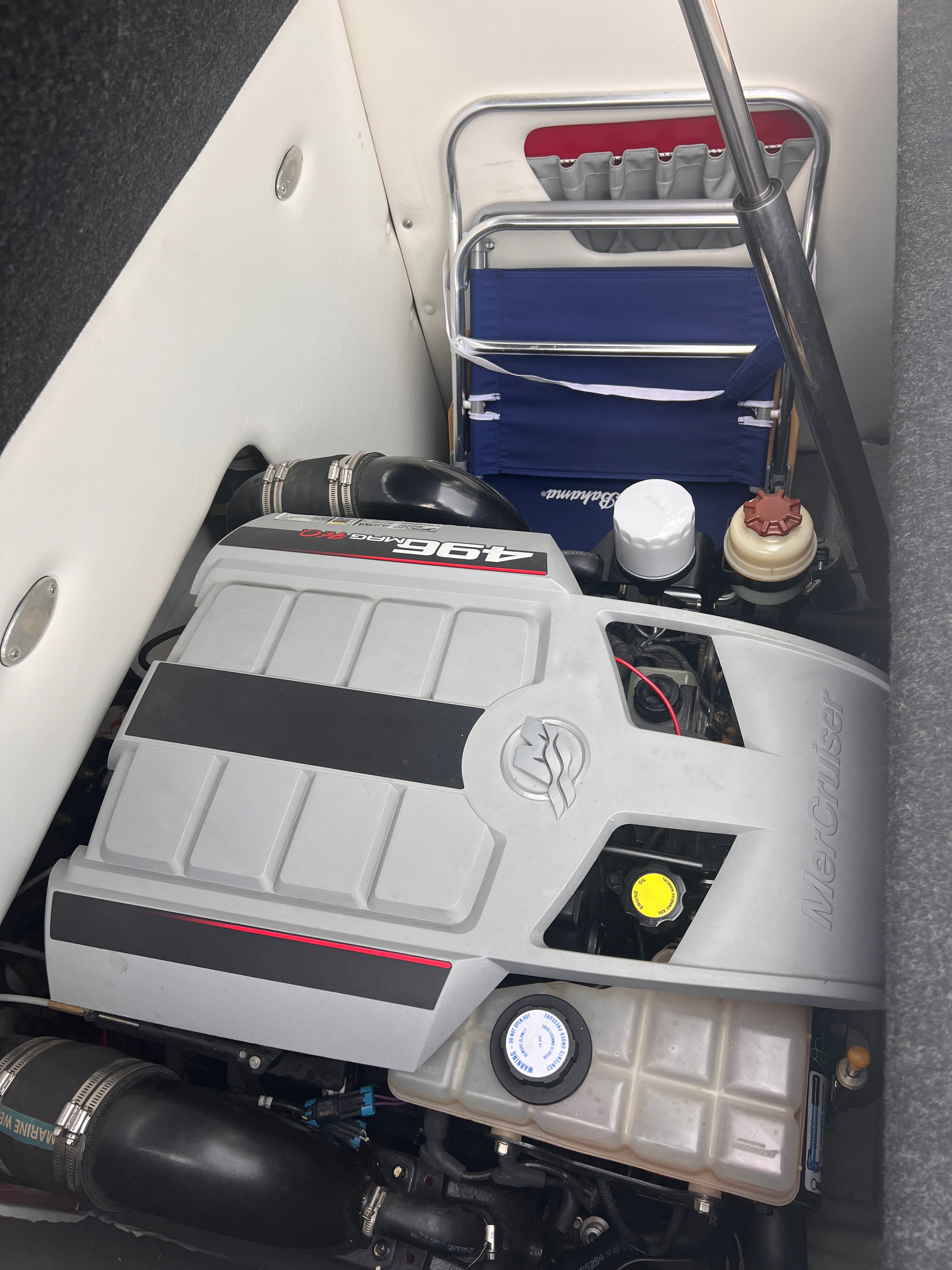 An engine compartment with a MerCruiser engine and a foldable blue chair.