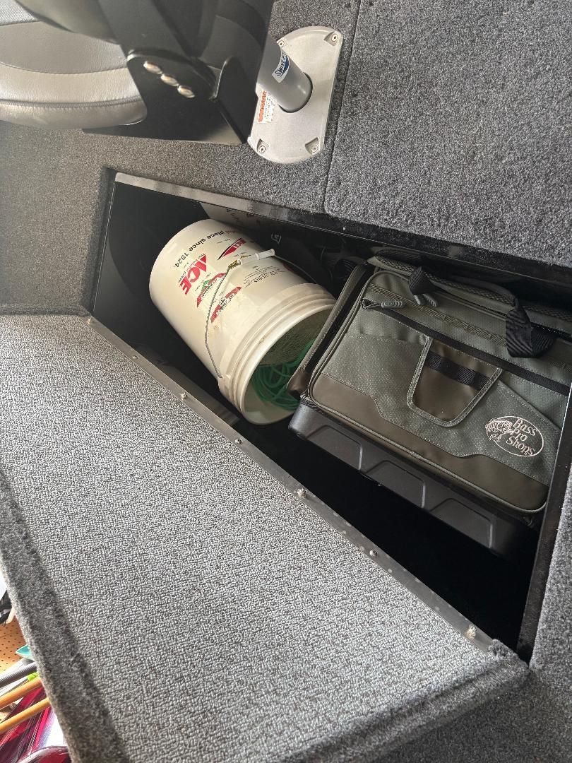 A storage compartment in the boat with a bucket and a bag.