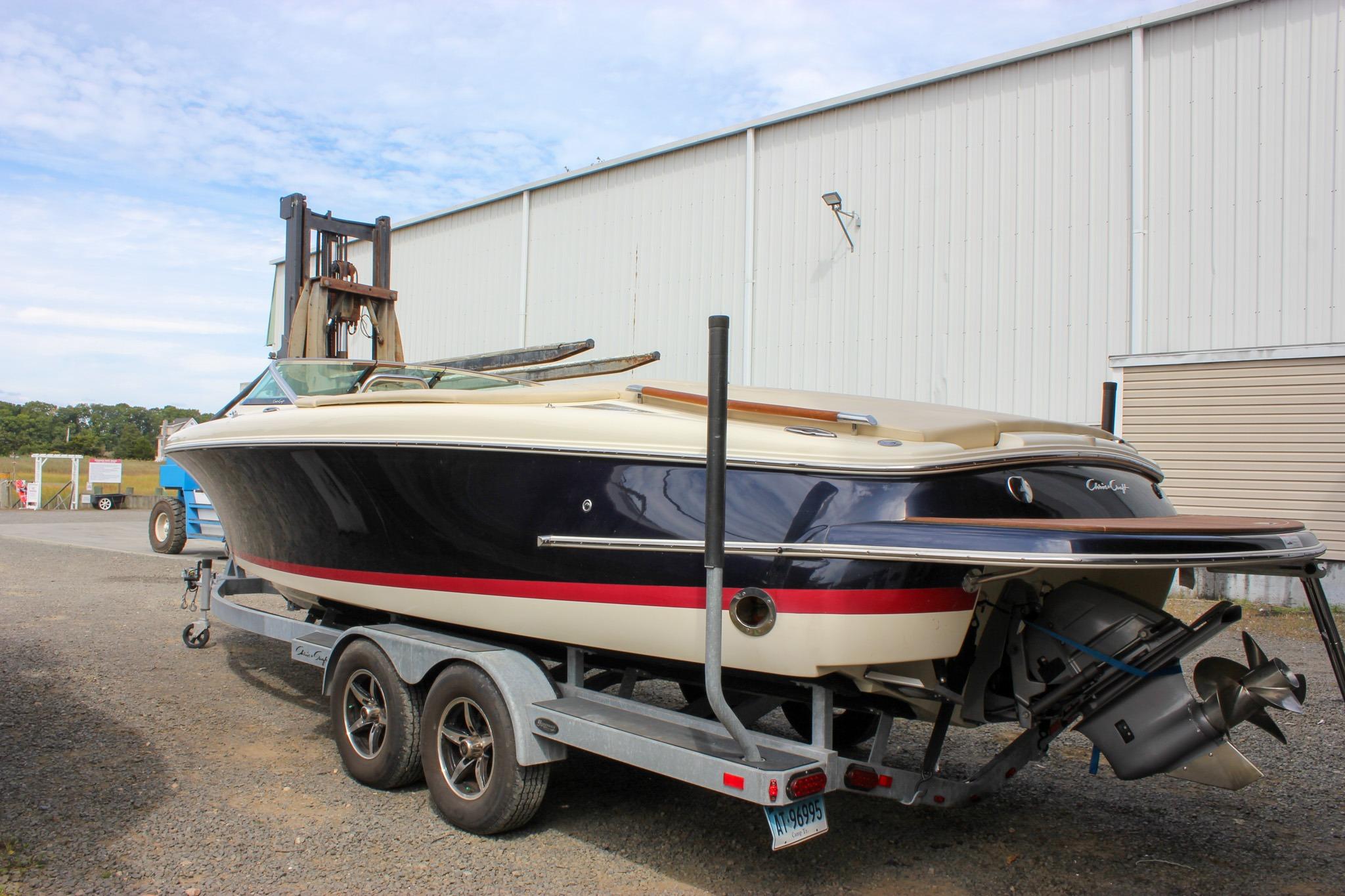 2017 Chris-Craft Capri 27 boat on trailer, parked outdoors near a warehouse.