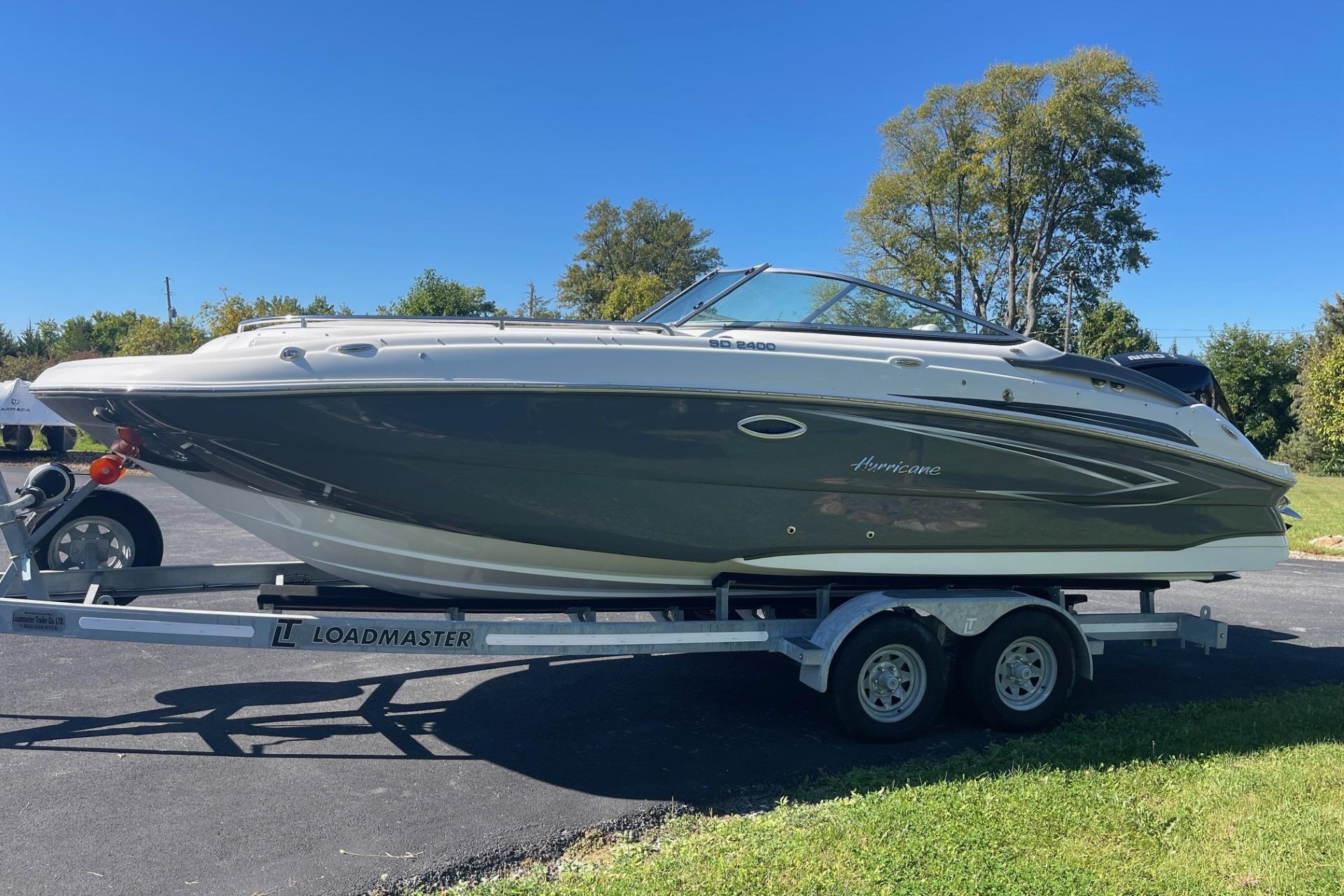 2023 Hurricane SunDeck 2400 OB boat on trailer, parked outdoors under clear blue sky.
