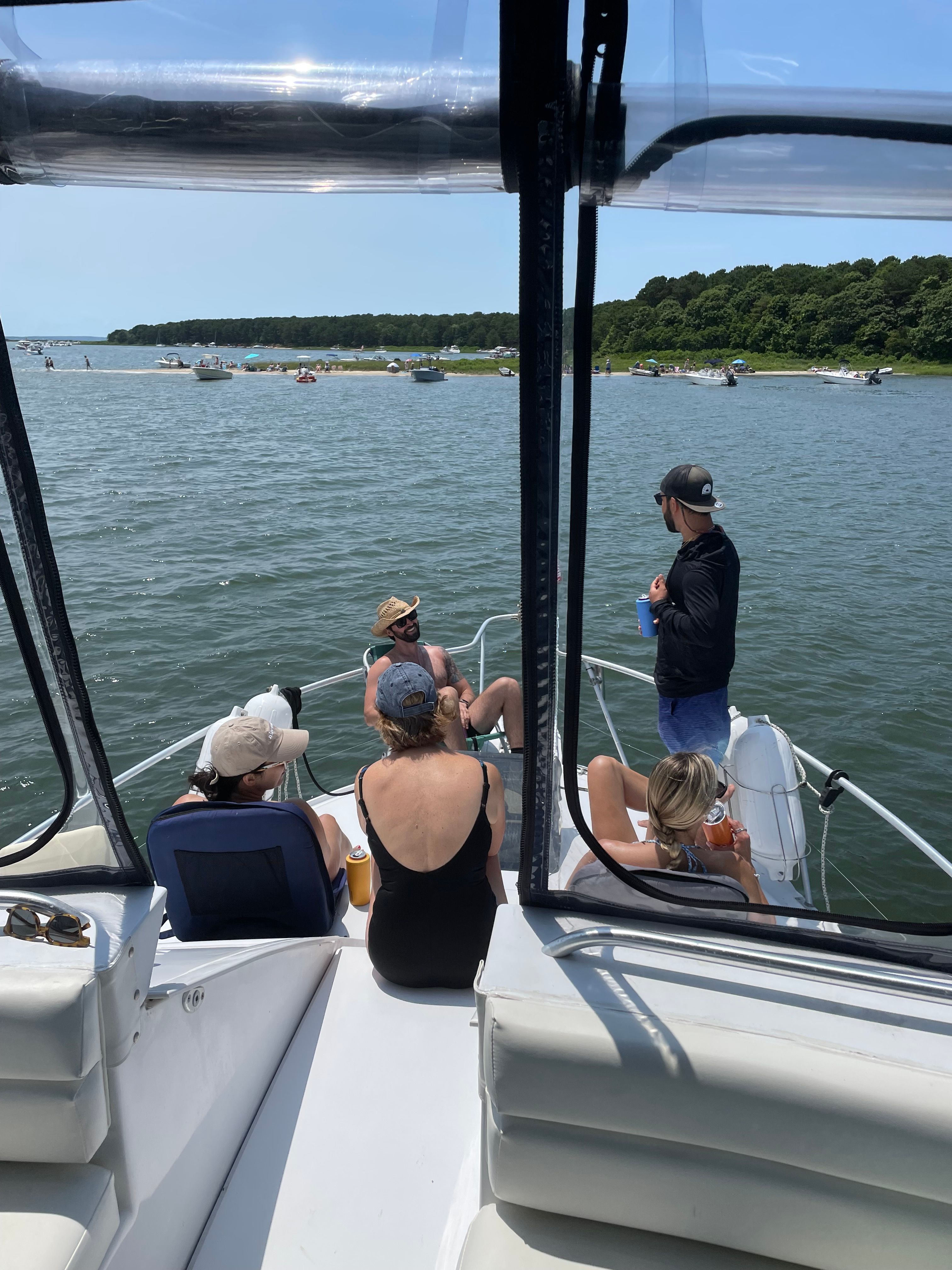 People relaxing on a boat on calm water, with trees in the background.