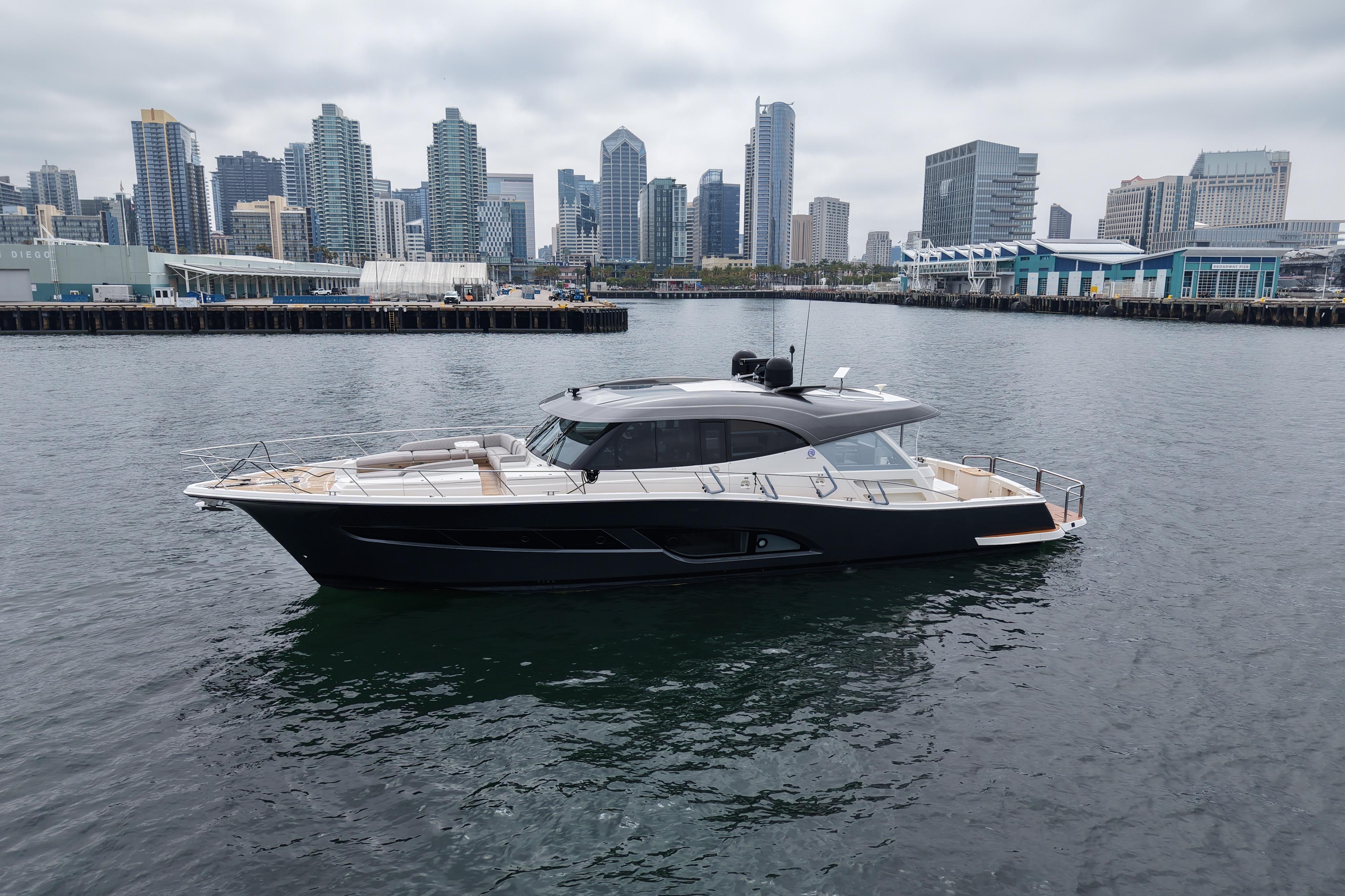 2023 Riviera 645 SUV yacht cruising in urban harbor with city skyline backdrop.