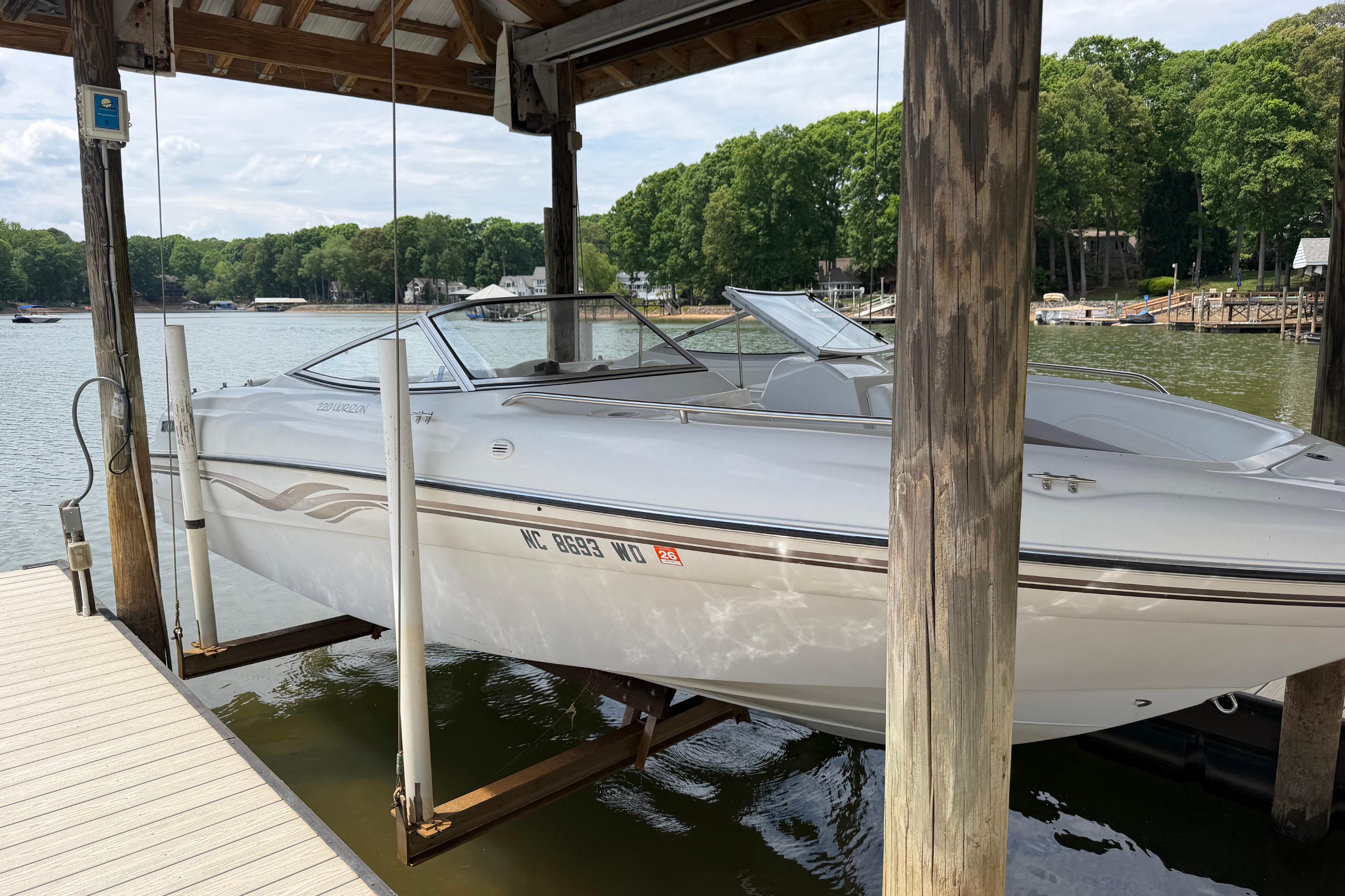 1998 Four Winns 220 Horizon boat docked on a lift by a scenic lake.