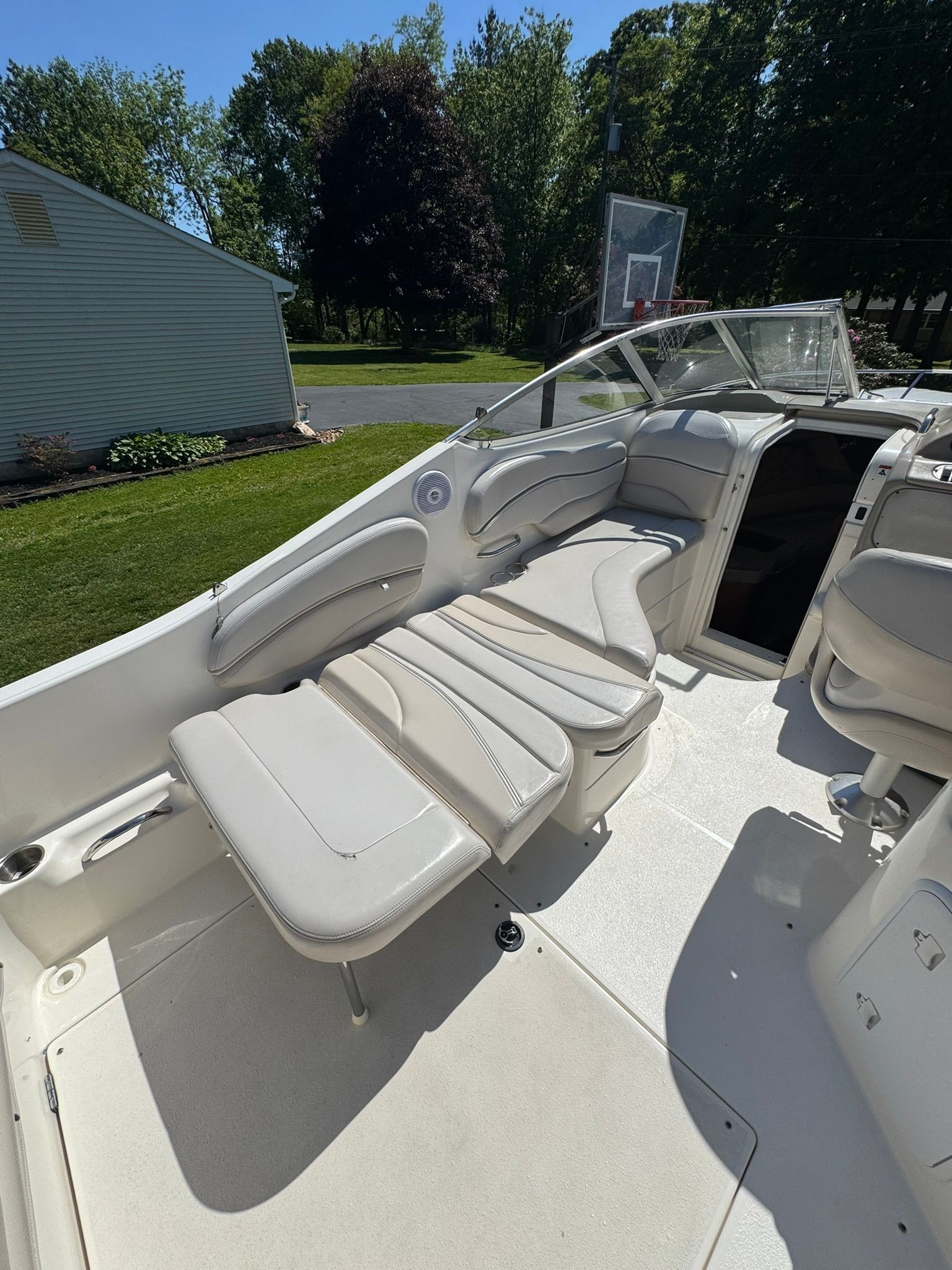 The boat has white cushioned seats and is parked in a garden.