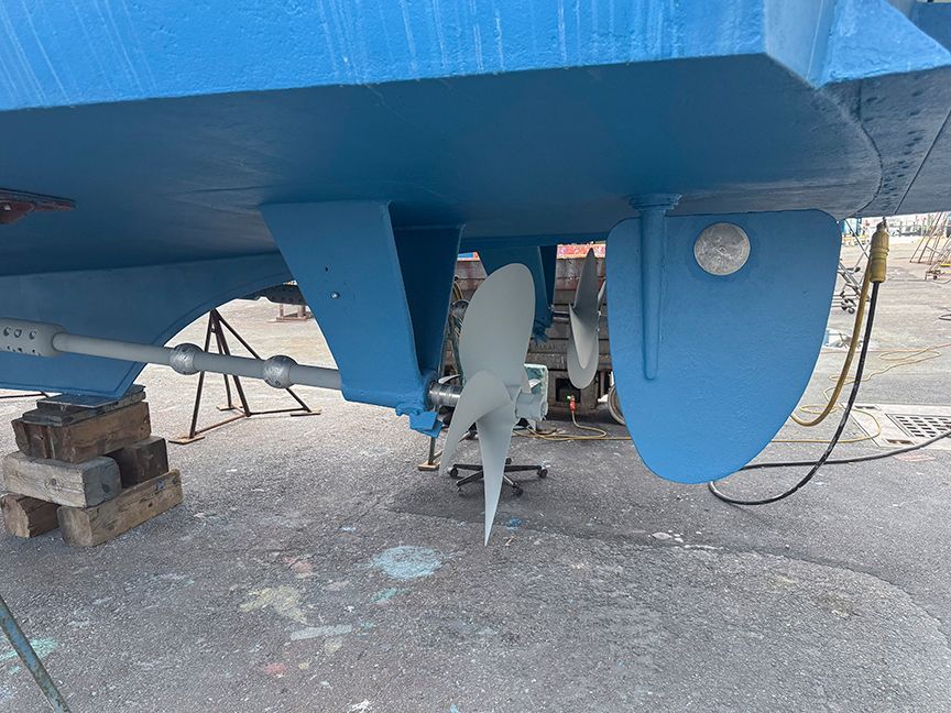 A blue-painted boat with visible propeller and rudder on a dry dock.
