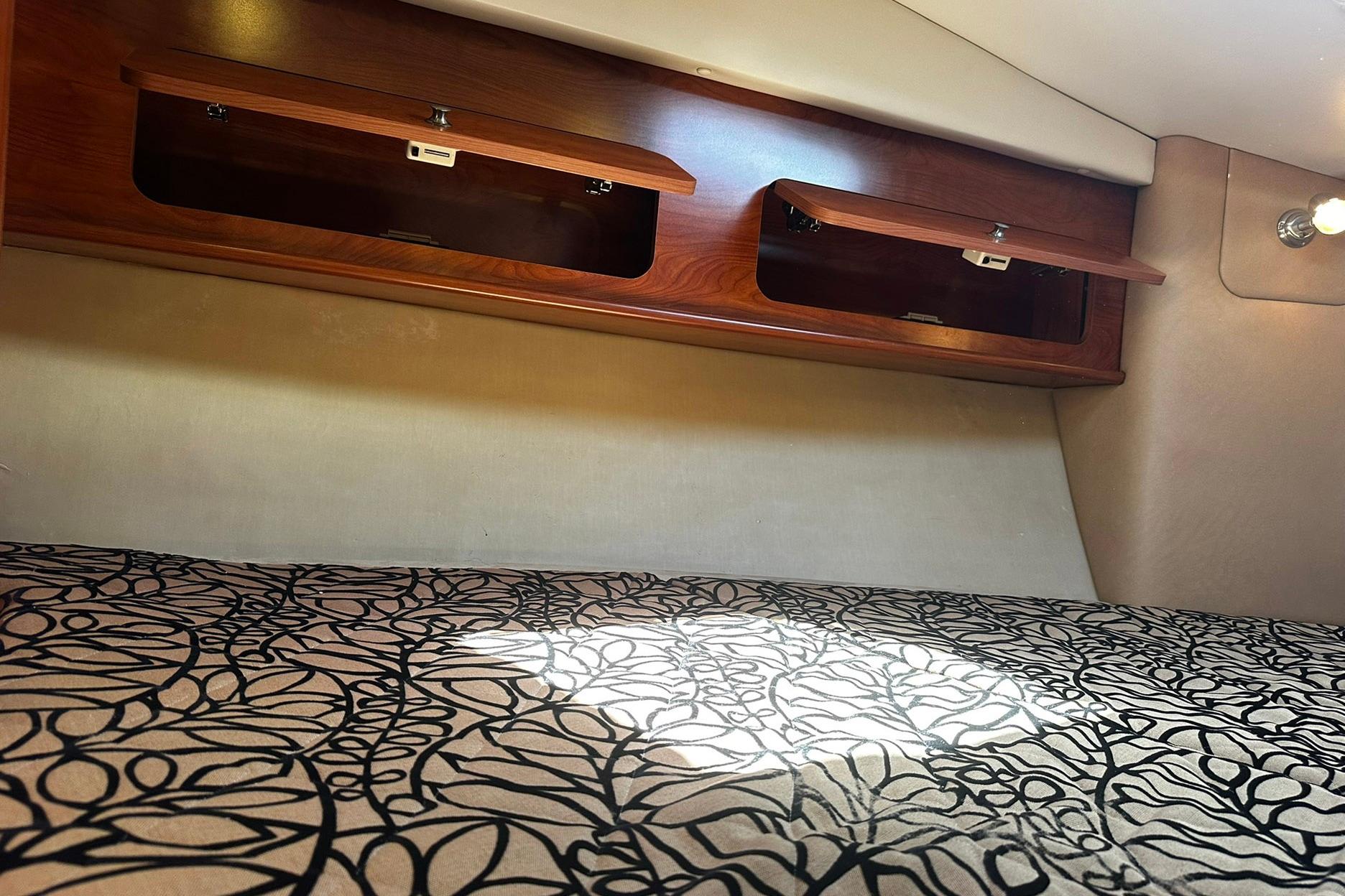 2012 Rinker 310 Express Cruiser LE cabin with patterned bedding and wooden storage compartments.