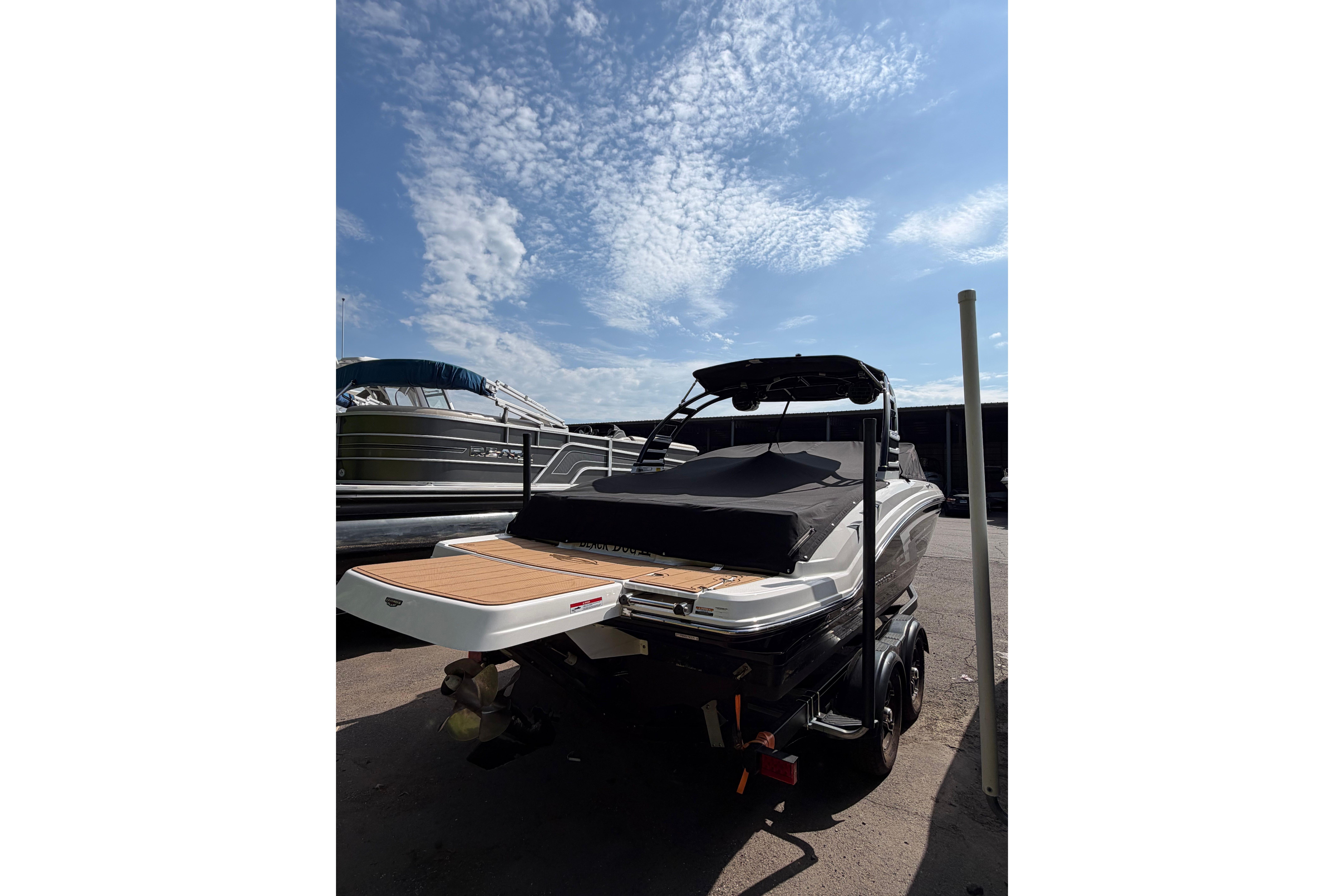 2025 Chaparral 230 SSi boat with covered deck, parked under a clear blue sky.