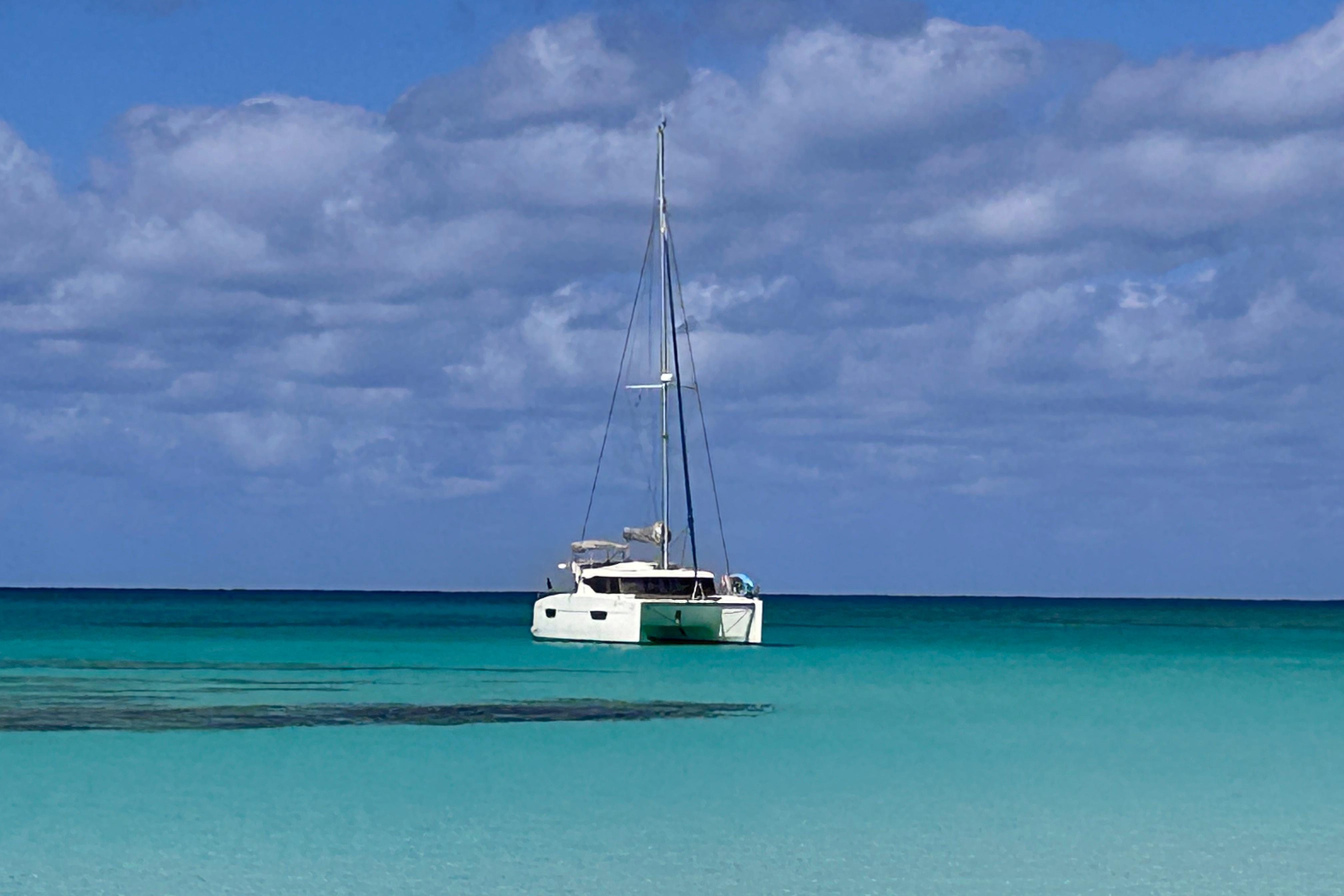 2018 Fountaine Pajot Lucia 40 catamaran sailing on turquoise ocean under cloudy sky.