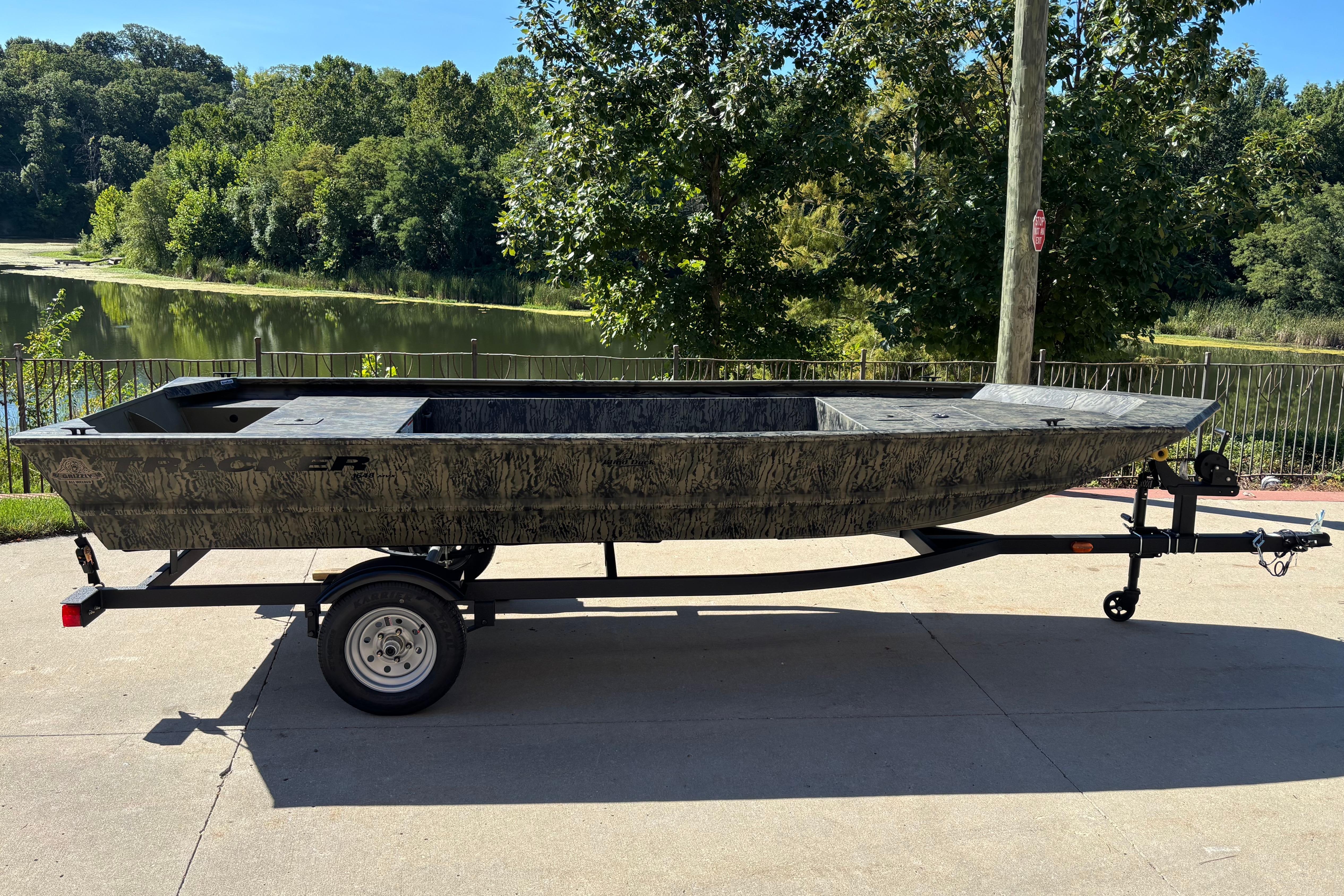 2026 Tracker Grizzly 1648 Utility boat on trailer by a scenic lake.