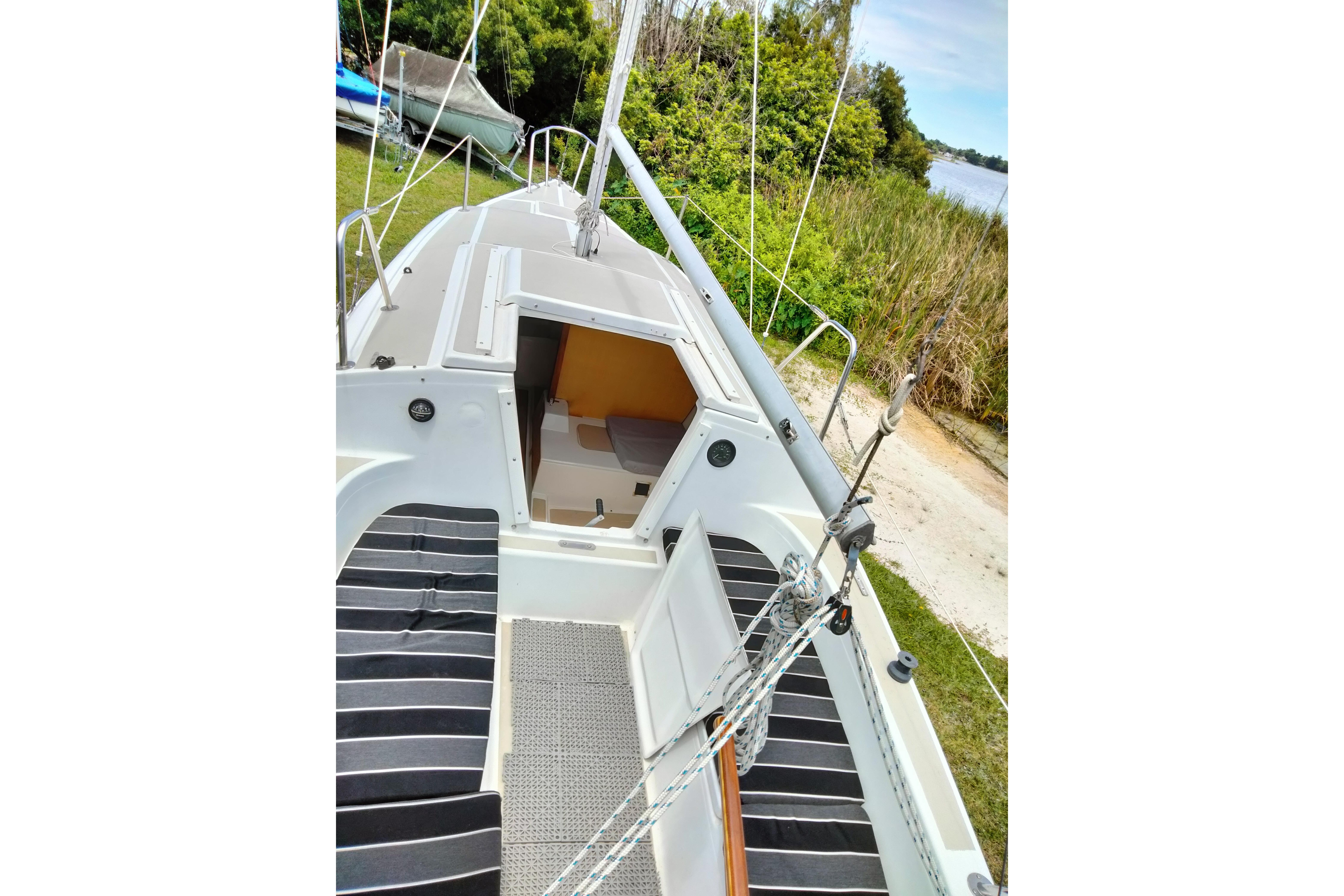1980 MacGregor 25 sailboat deck with open cabin, surrounded by lush greenery.