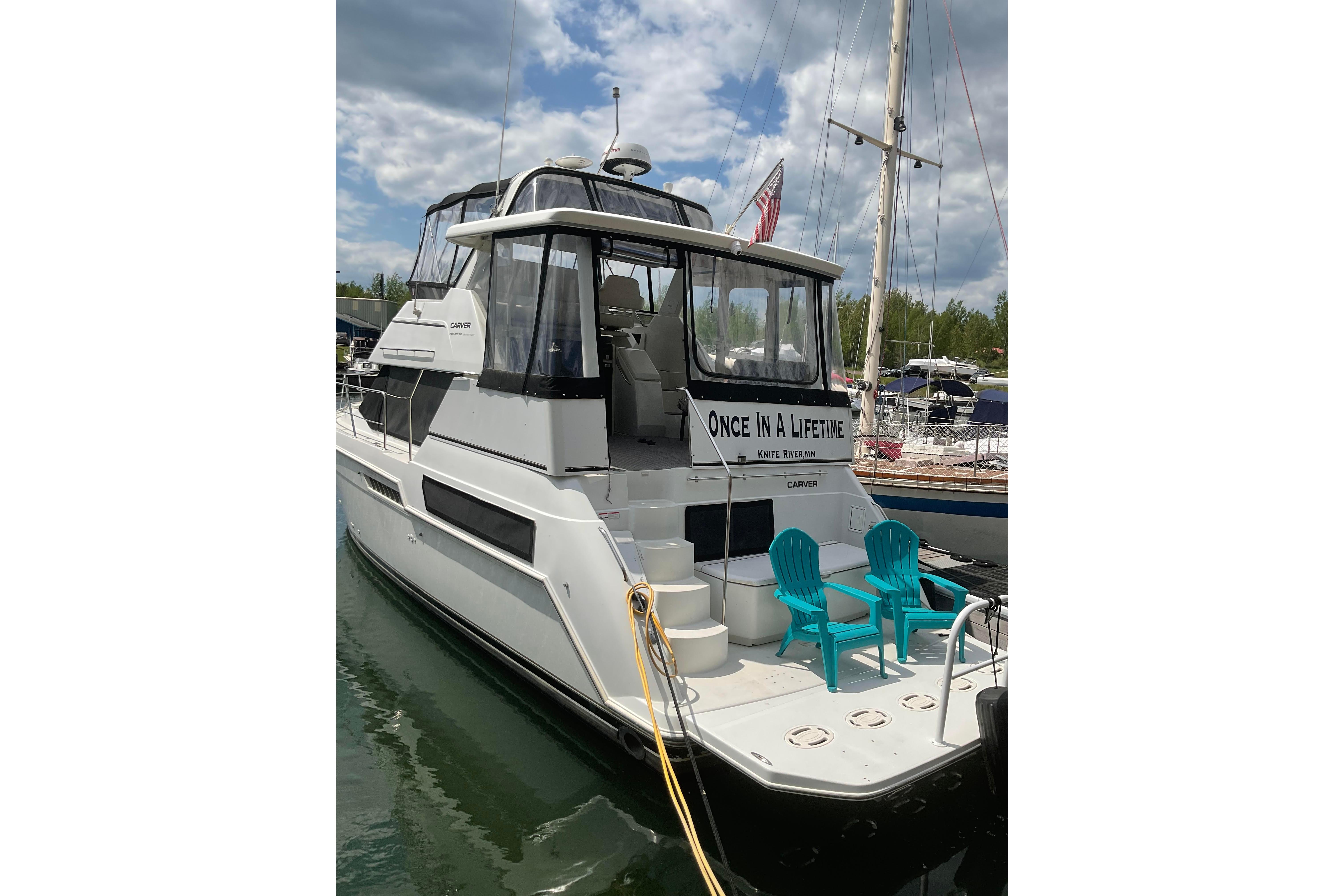 1998 Carver 355 Aft Cabin Motor Yacht docked, featuring outdoor seating and "Once In A Lifetime" signage.