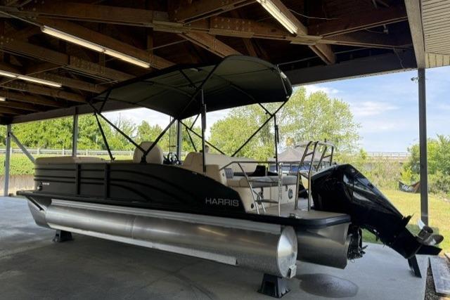 2025 Harris Sunliner 230 pontoon boat under a wooden shelter, featuring a sleek black design.