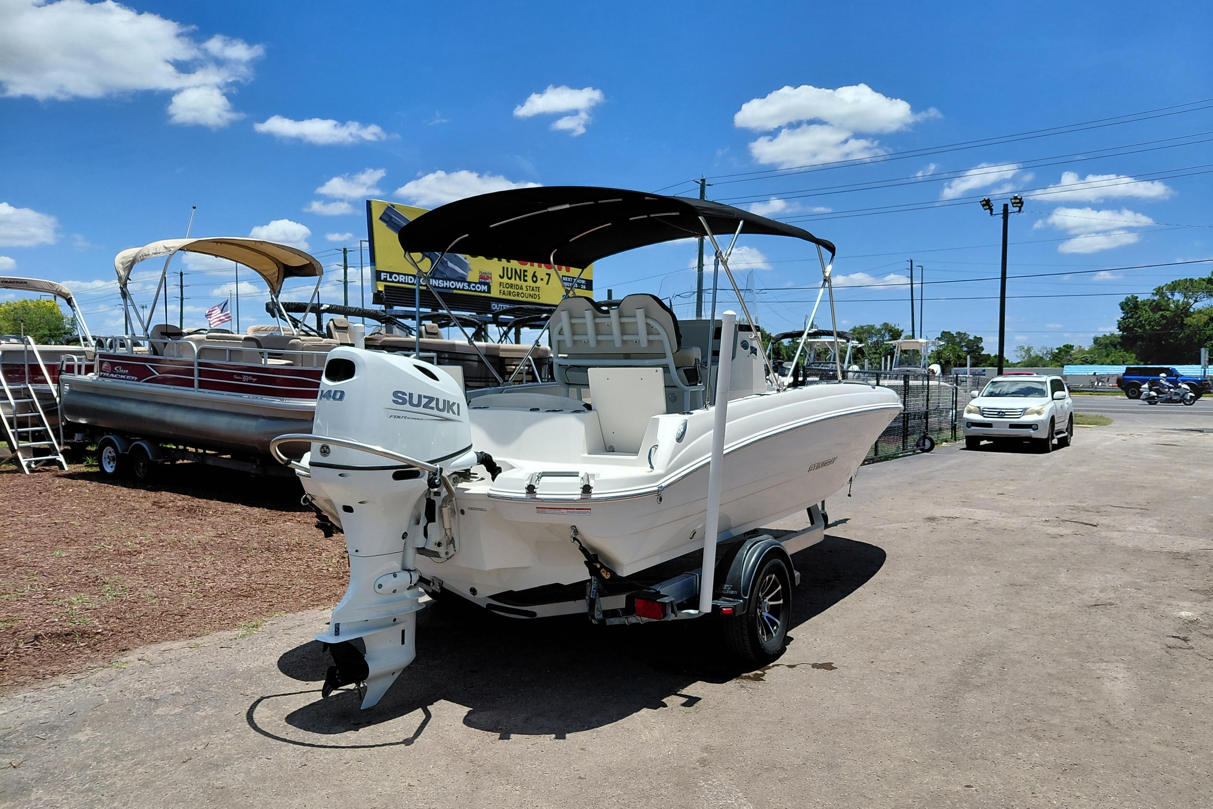 2023 Stingray 206 CC boat with Suzuki engine, parked outdoors under a clear blue sky.