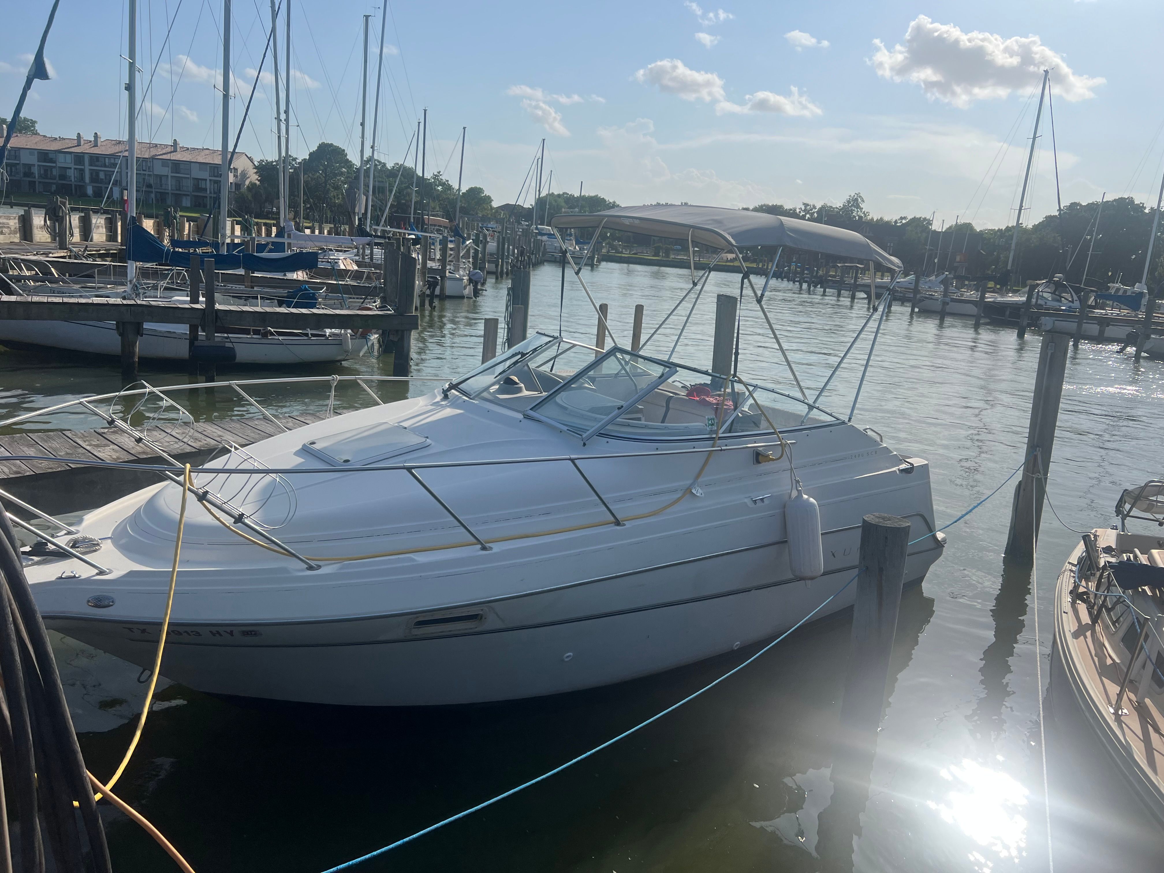 A white boat is docked in a sunny harbor, surrounded by other boats and yachts.