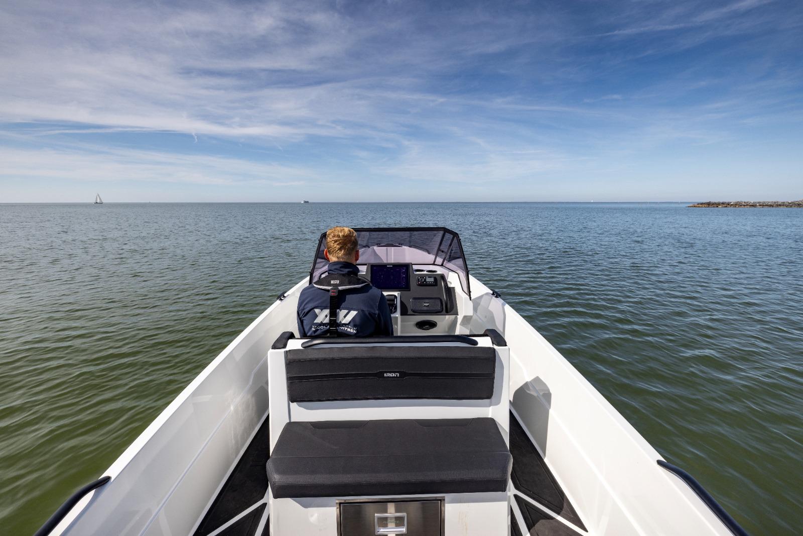 A person steering an Iron 707 boat on open water under a clear sky.