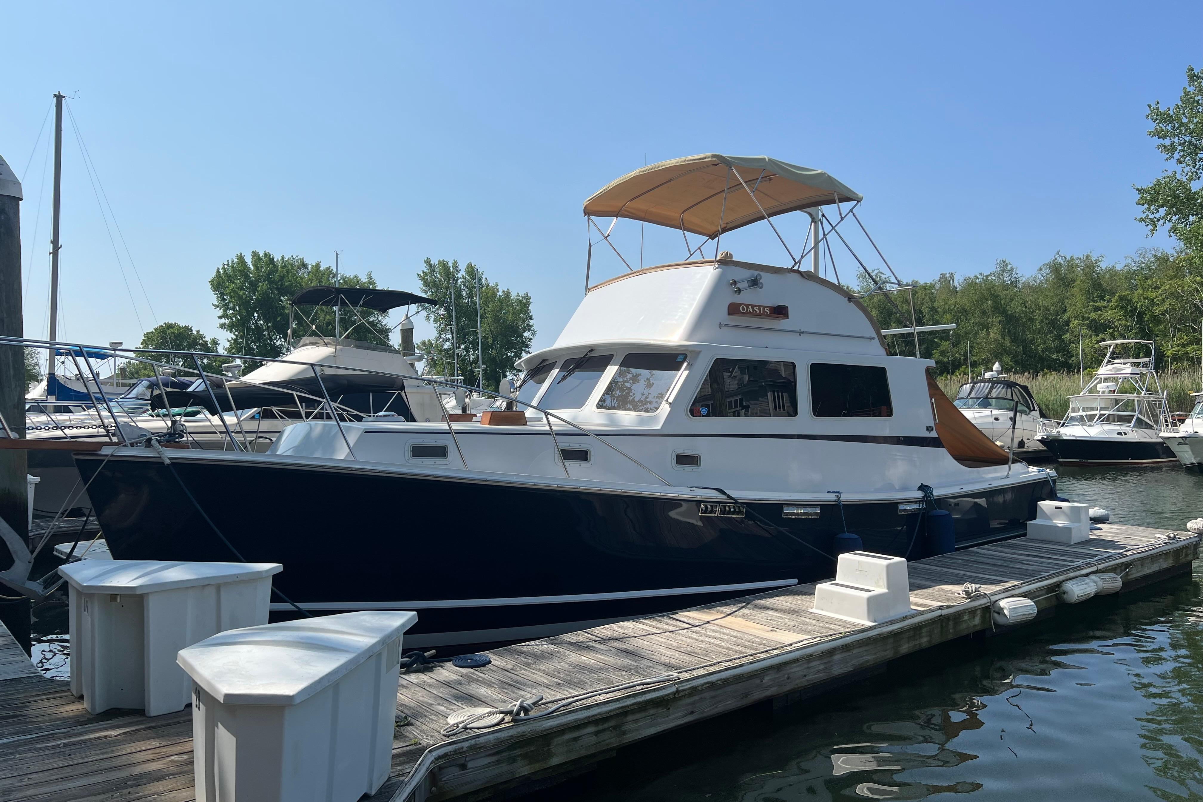 1987 Wilbur 38 boat docked at marina, featuring a blue hull and tan canopy.
