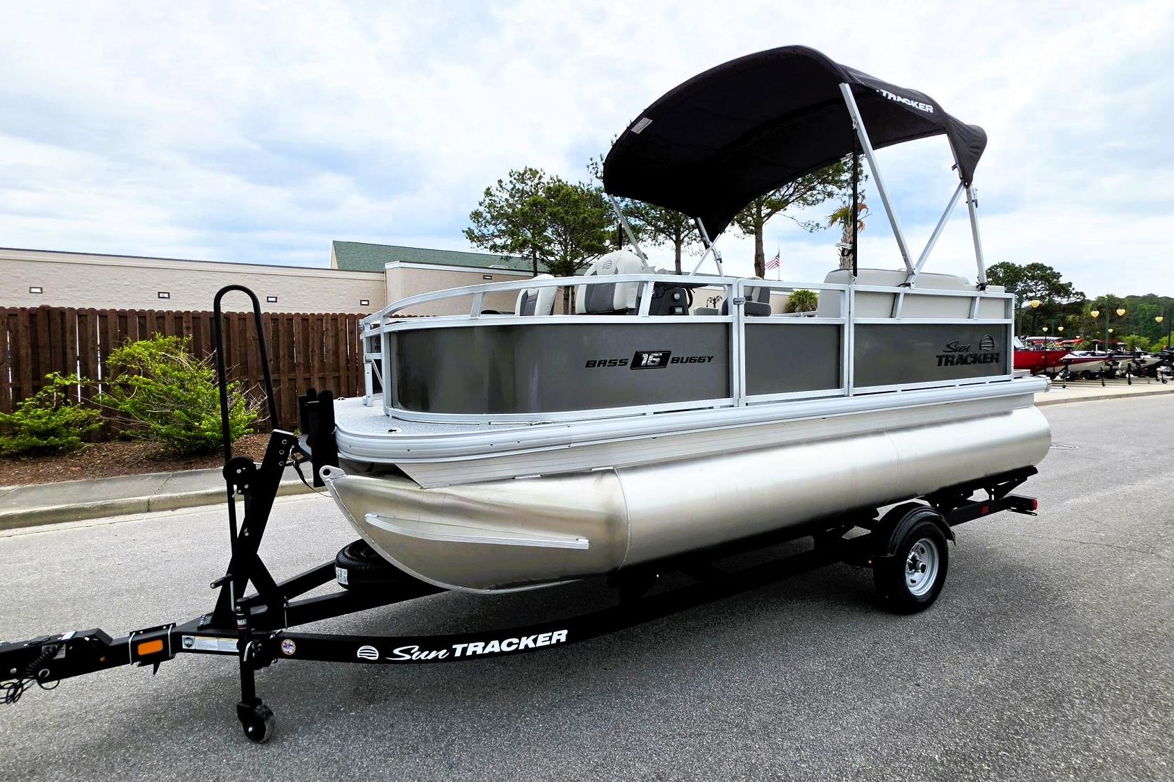2026 Sun Tracker Bass Buggy 16 XL Select pontoon boat on trailer, parked outdoors.