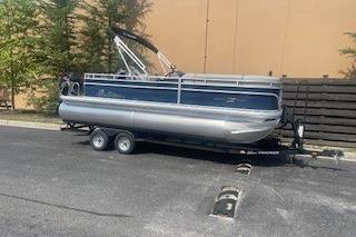 2026 Sun Tracker SportFish 20 DLX pontoon boat on trailer in parking lot.