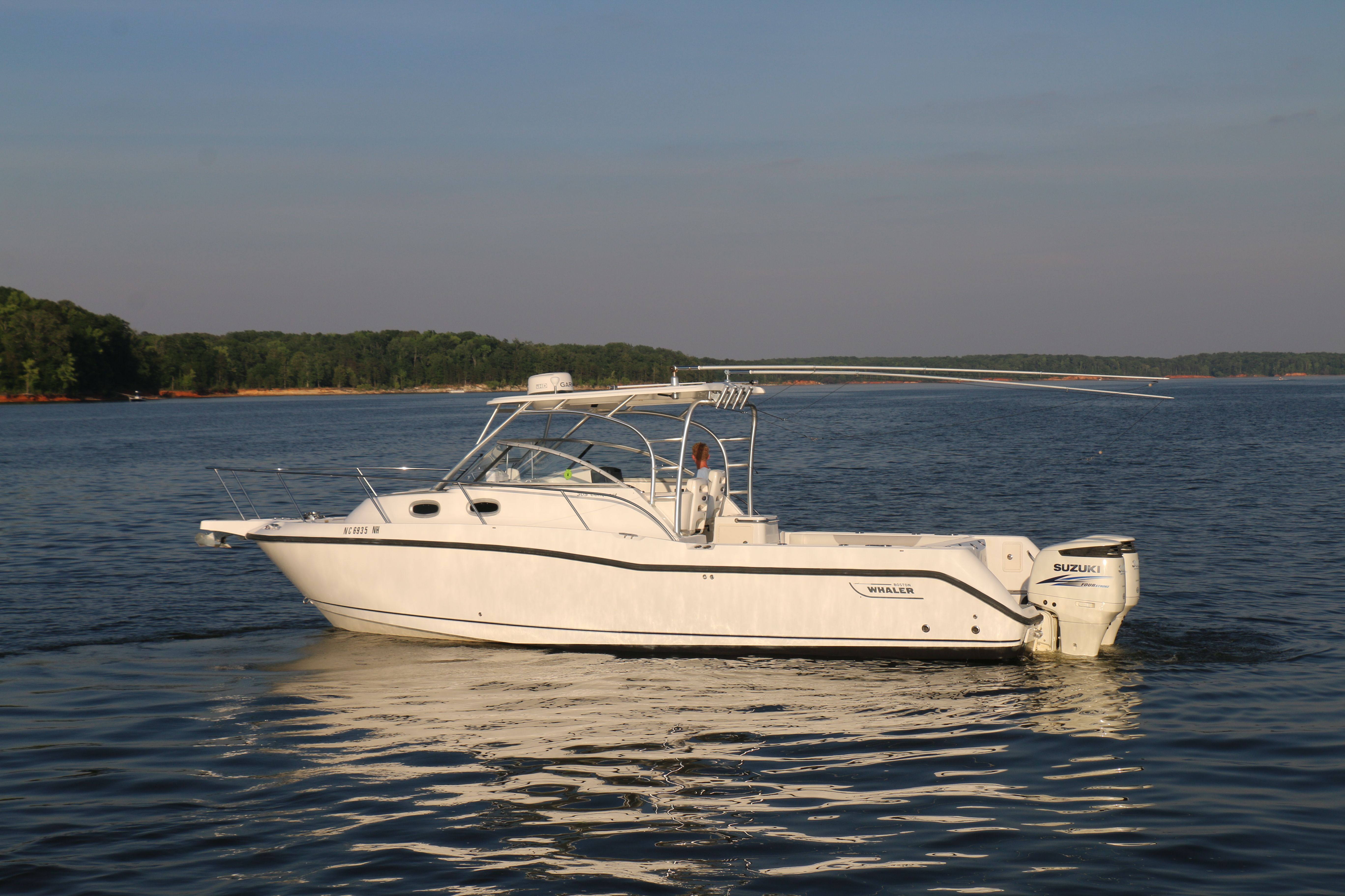 A 2006 Boston Whaler 305 Conquest on calm water with a wooded shoreline in the background.