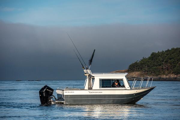 2023 Spartan 220 Maximus Pro boat on calm water near forested shoreline.