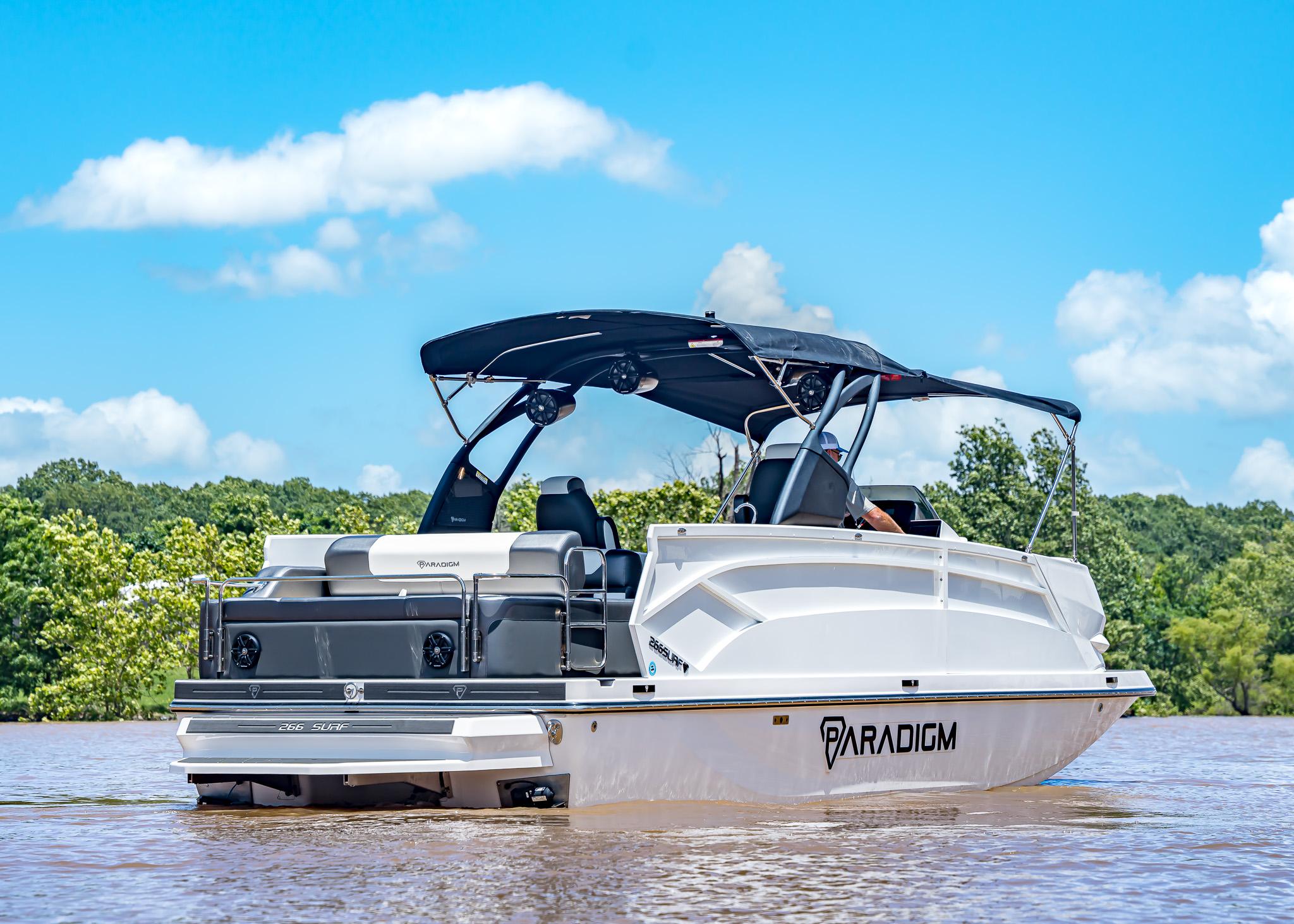 2025 Paradigm Damascus 266 Surf boat on a sunny lake, featuring sleek design and canopy.
