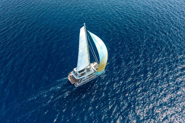Aerial view of 2025 Lagoon 60 sailing on open blue sea.