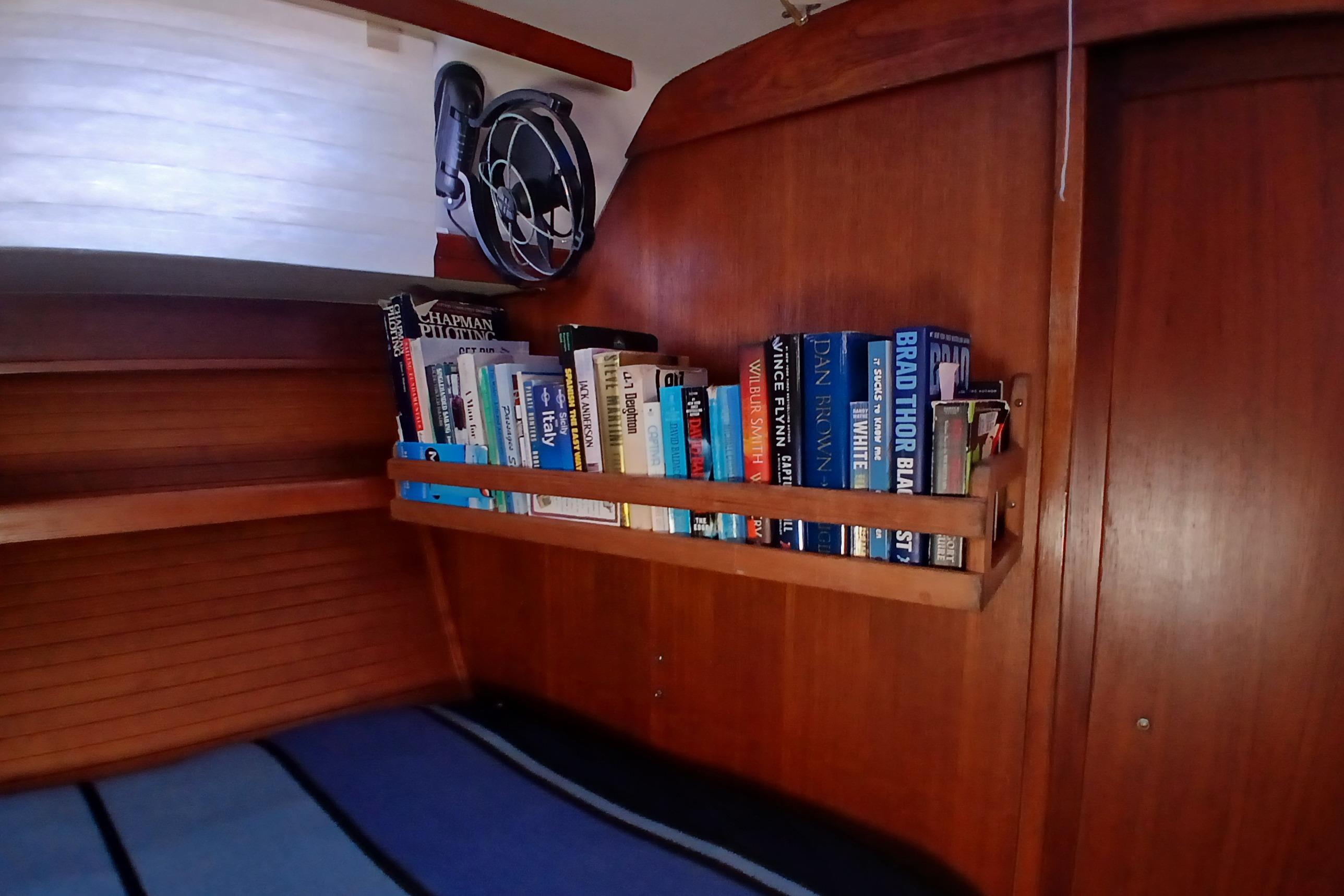 Bookshelf in a 1995 Catalina 42 MkII yacht cabin with fan and wooden interior.