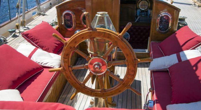 Vintage 1931 schooner sailboat helm with wooden wheel and red cushioned seating.