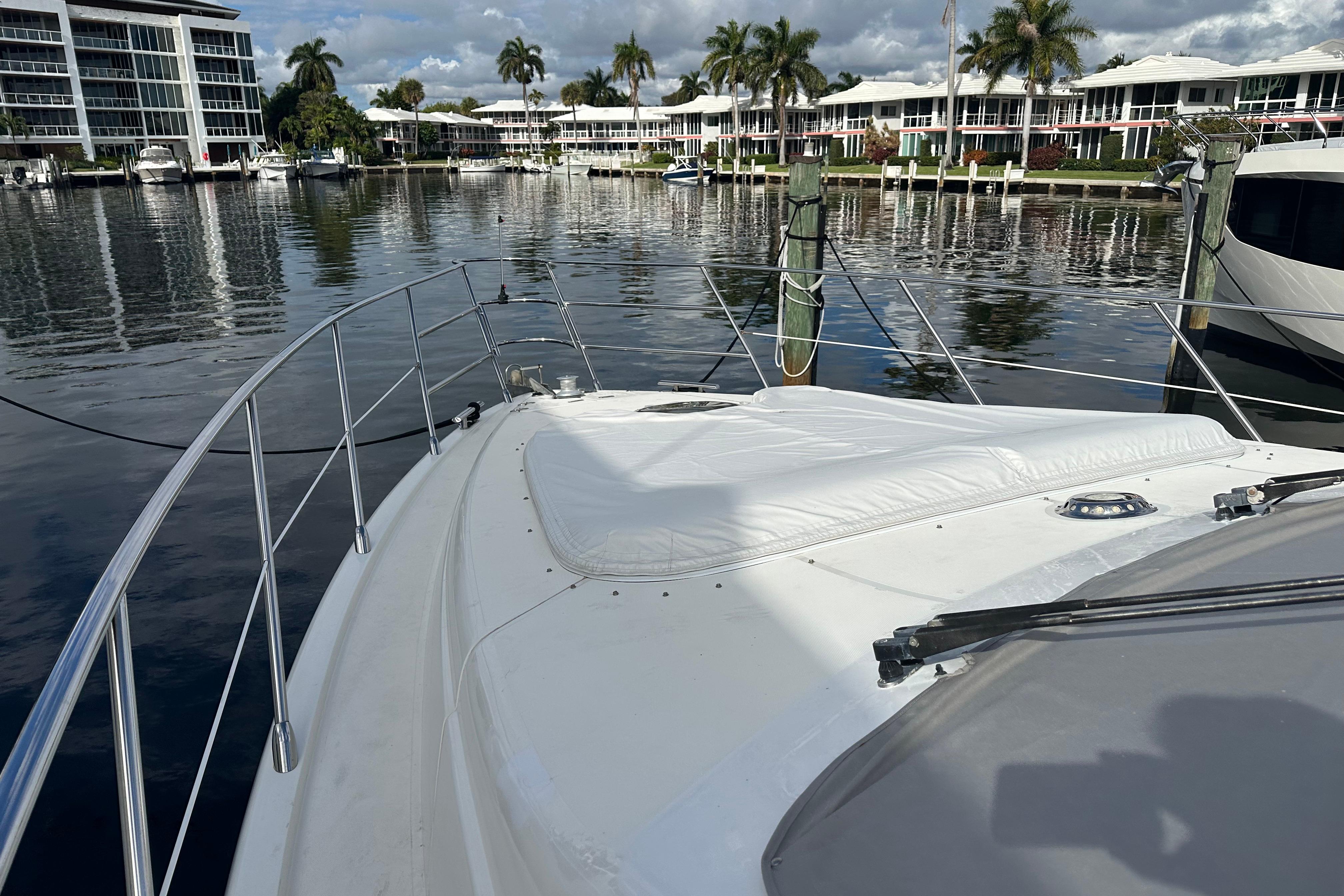 2004 Azimut 55E yacht docked in a serene marina with palm trees and waterfront buildings.