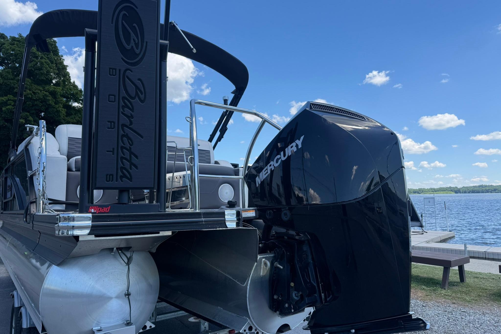 2023 Barletta Corsa 23U pontoon boat with Mercury engine by a lakeside.