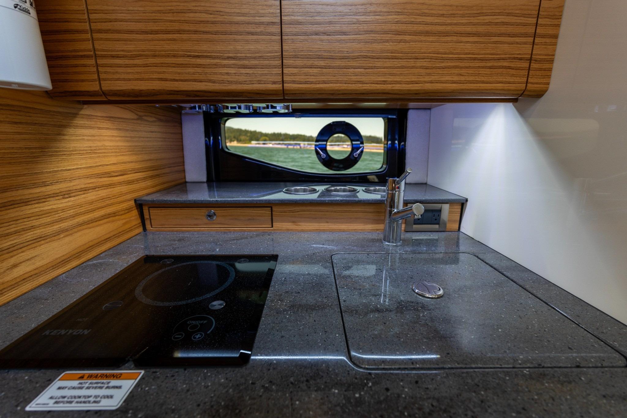 Modern kitchen area in 2023 Boston Whaler 405 Conquest boat, featuring sleek countertops and wood cabinetry.