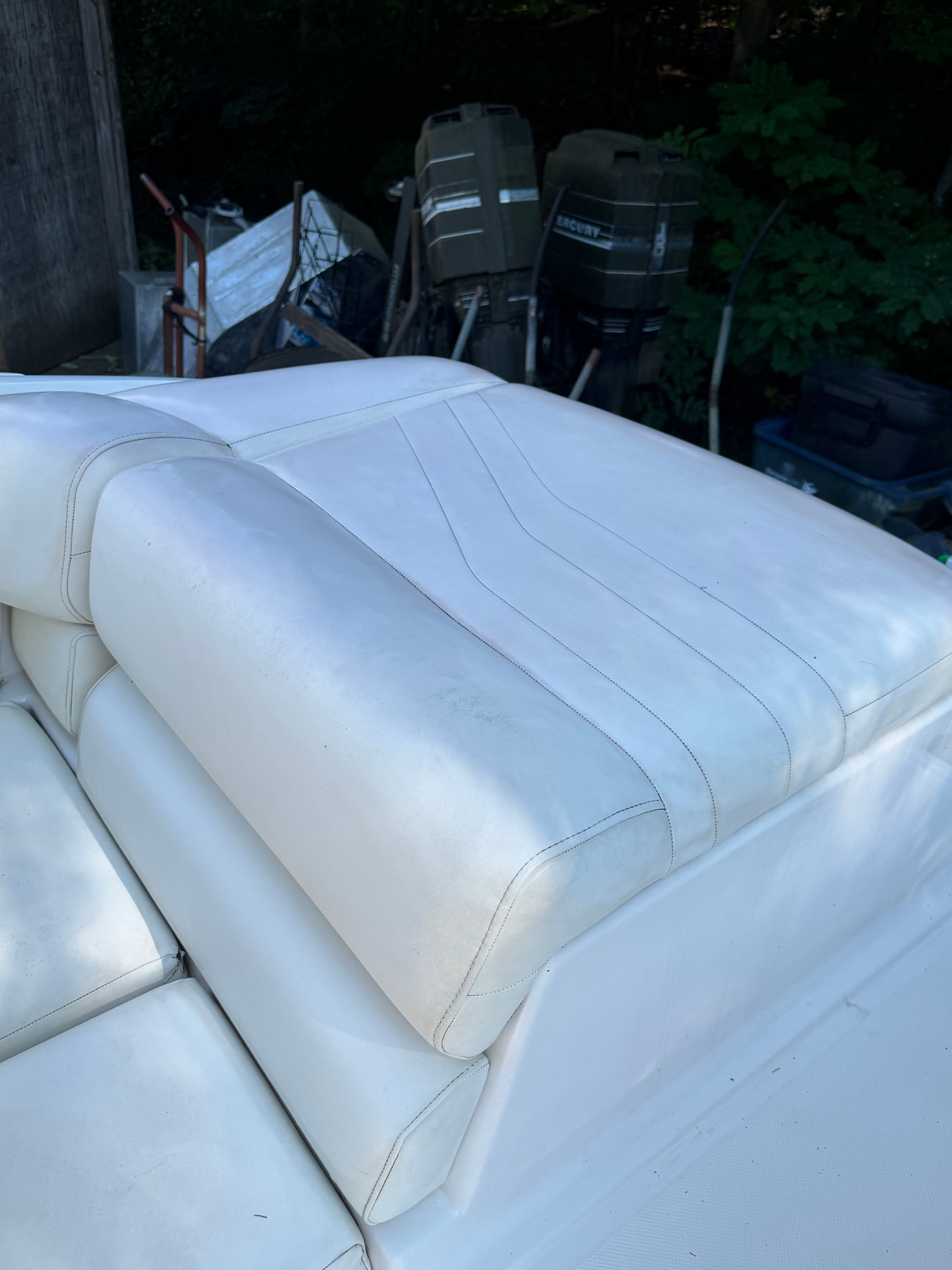 White upholstery on a boat seat with clean stitching, surrounded by trees and equipment.