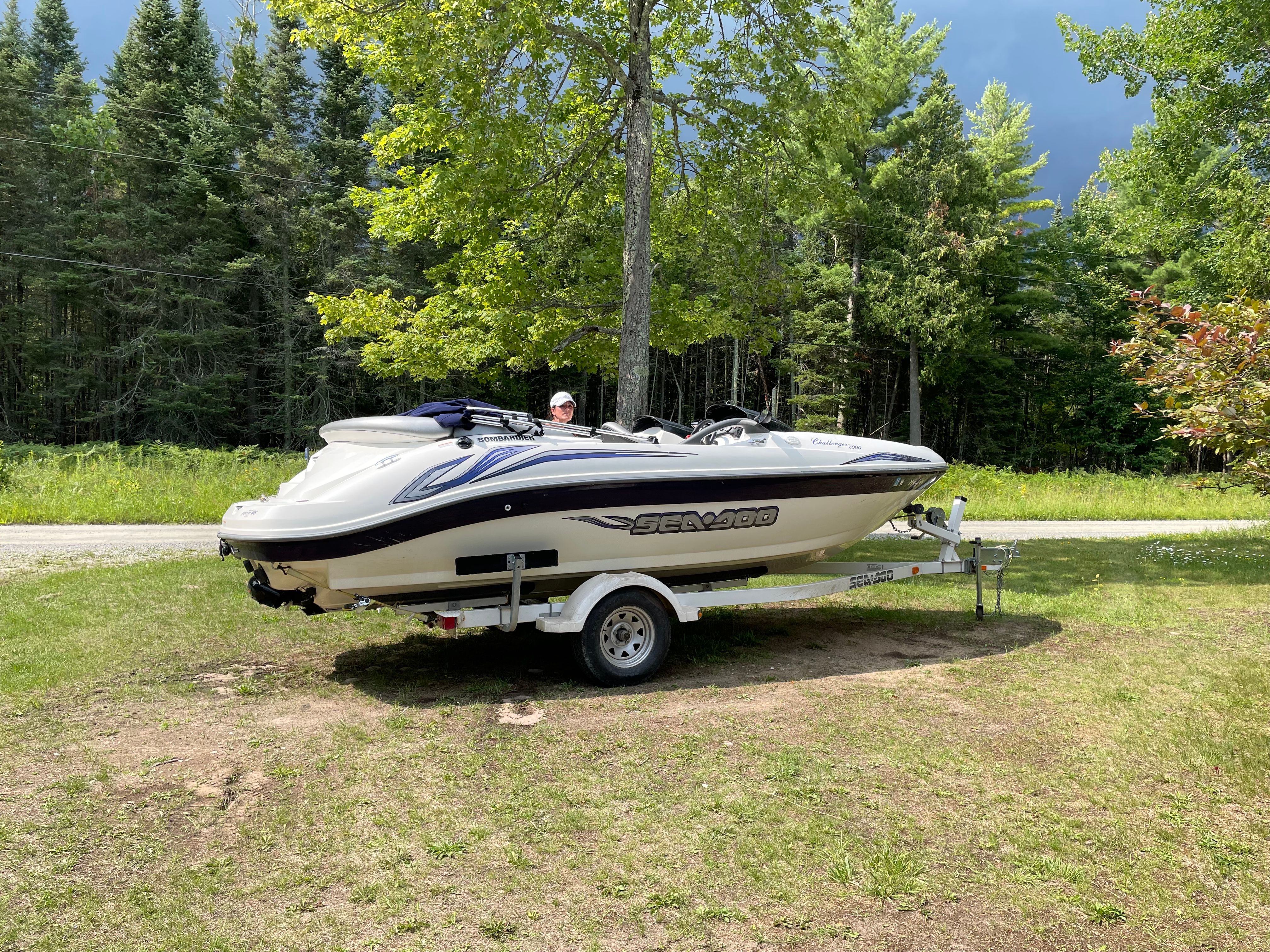 2004 Bombardier Challenger boat on trailer, surrounded by lush green trees.