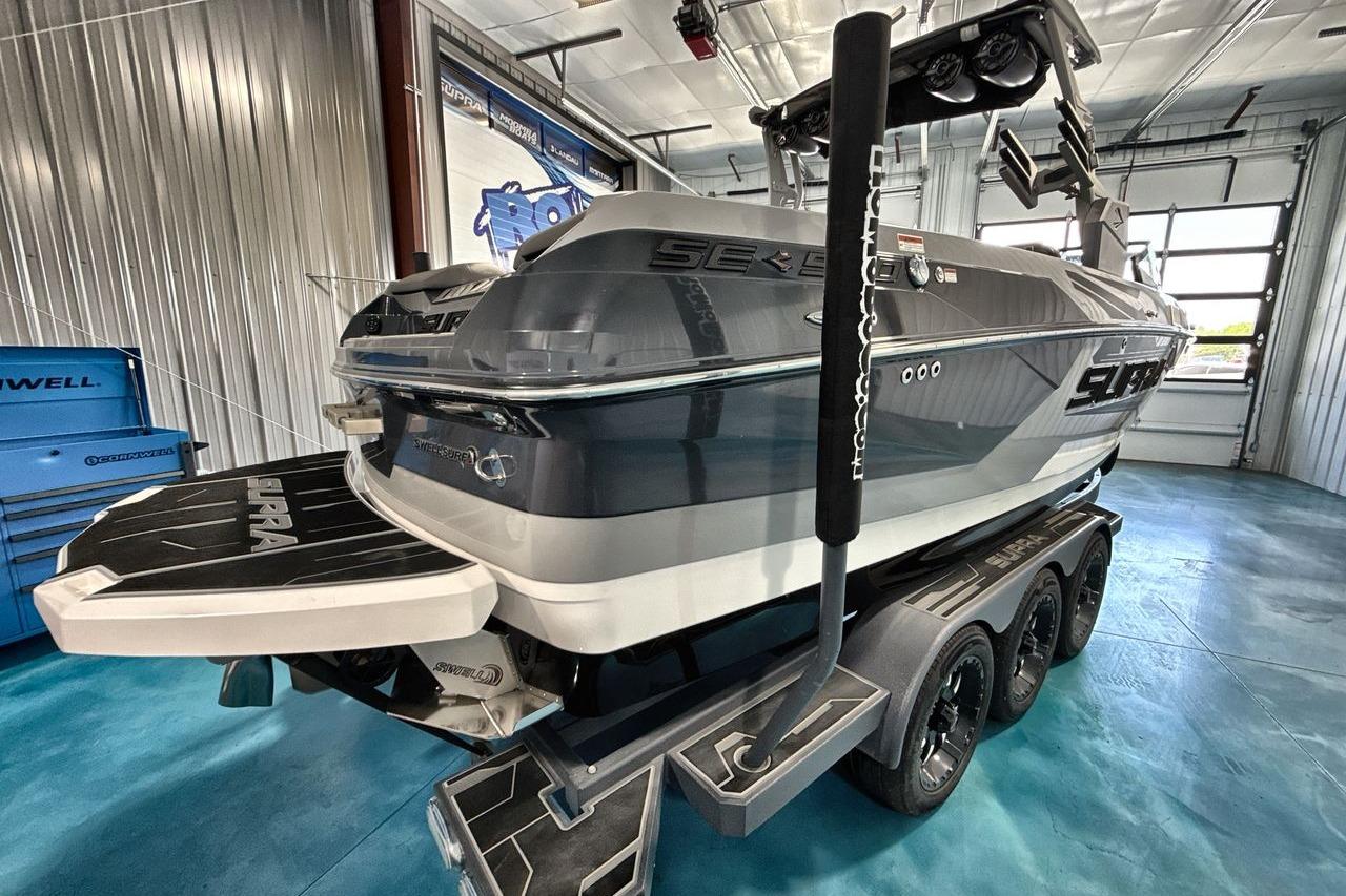 2021 Supra SE 550 boat in showroom, featuring sleek design and triple-axle trailer.