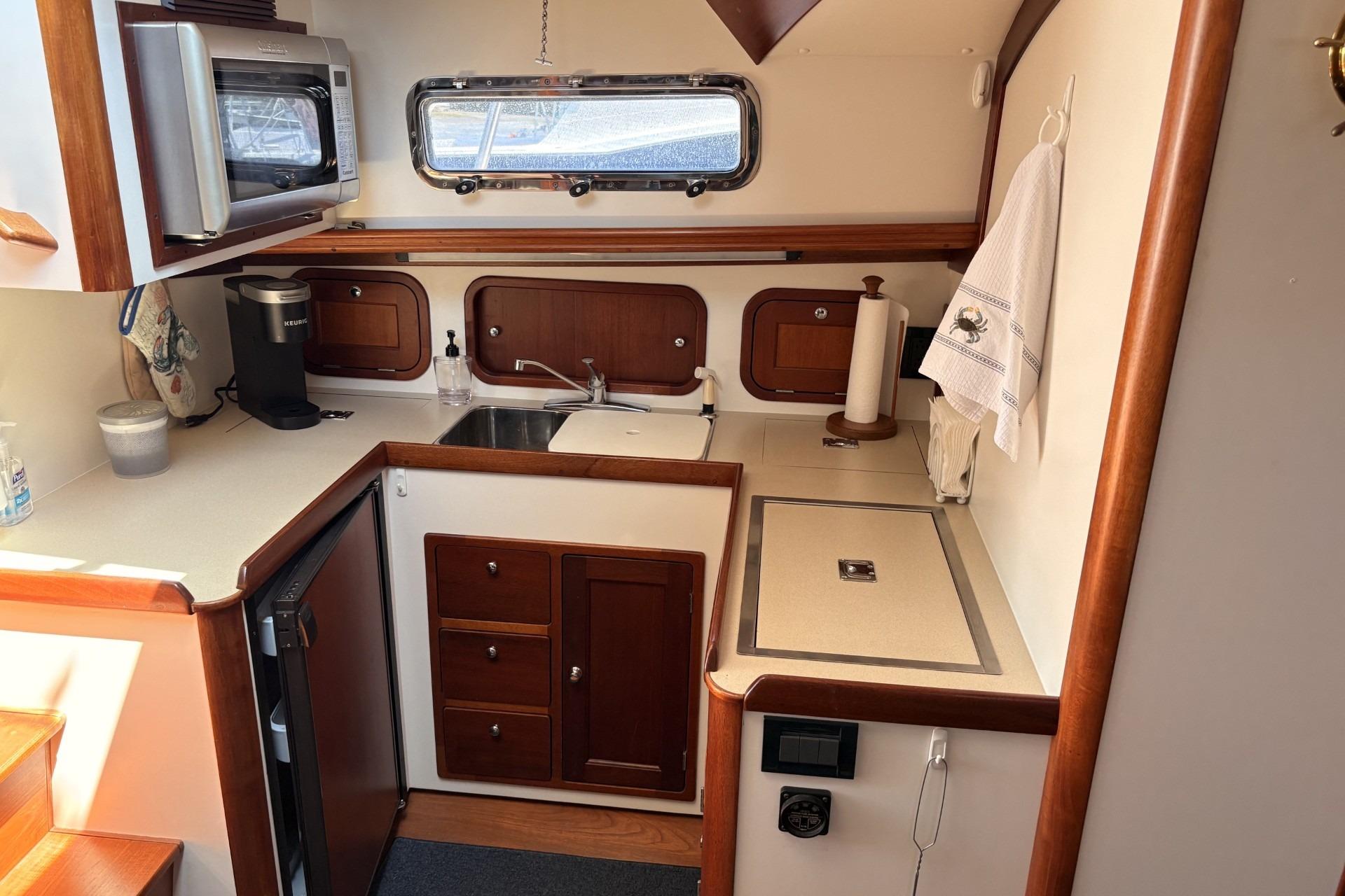 Compact boat kitchen with wooden cabinets, microwave, sink, and coffee maker.