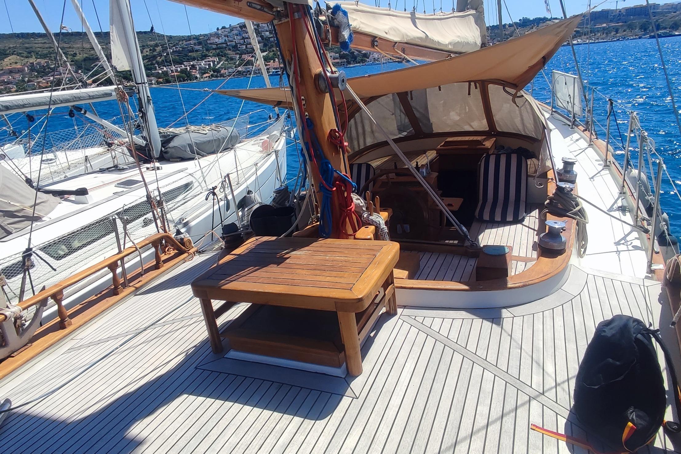 1980 Formosa 51 sailboat deck with wooden table, striped cushions, and scenic ocean view.