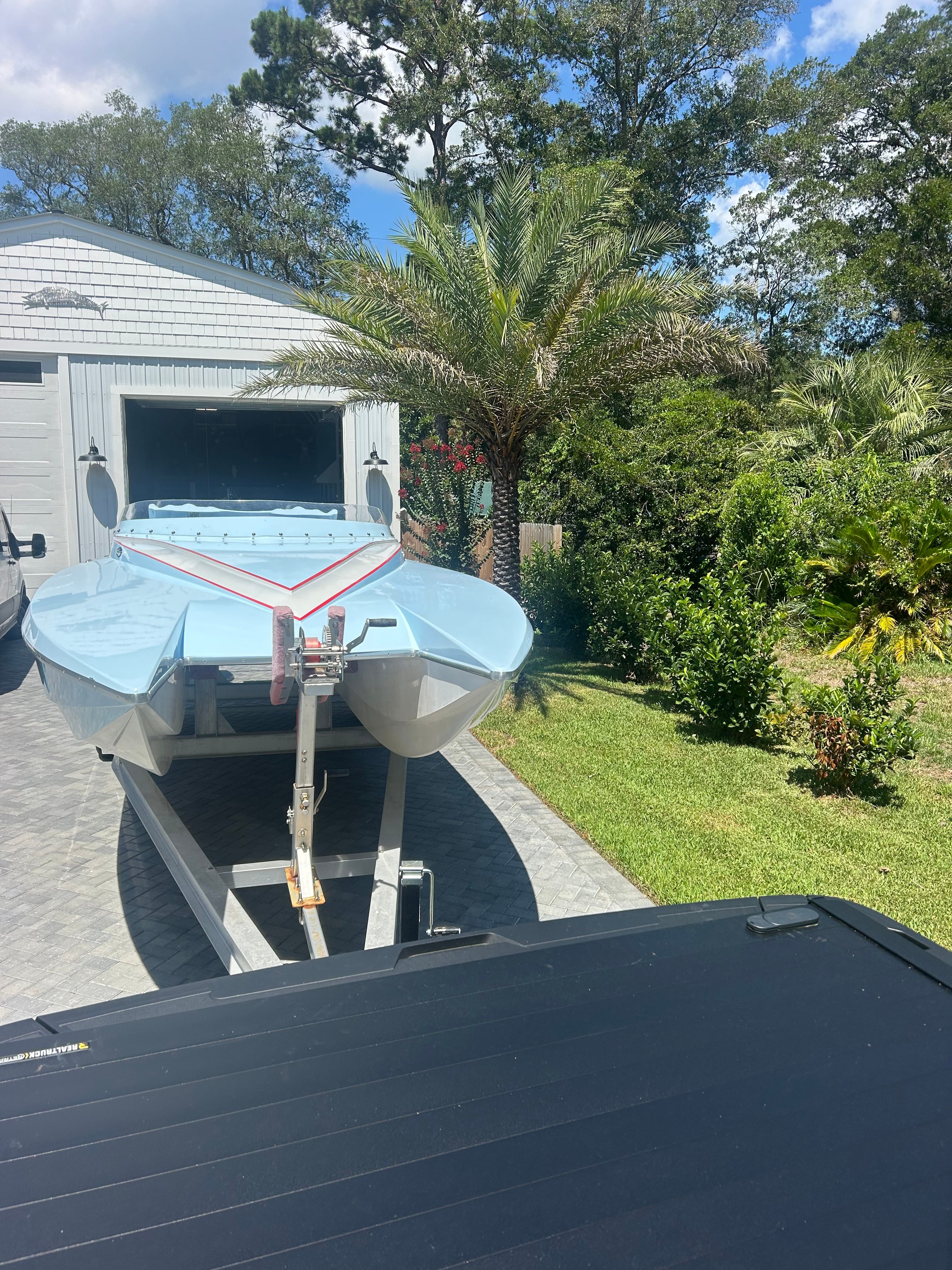 A 1992 Motion Marine 25 CAT boat on a trailer in front of a garage, surrounded by trees.