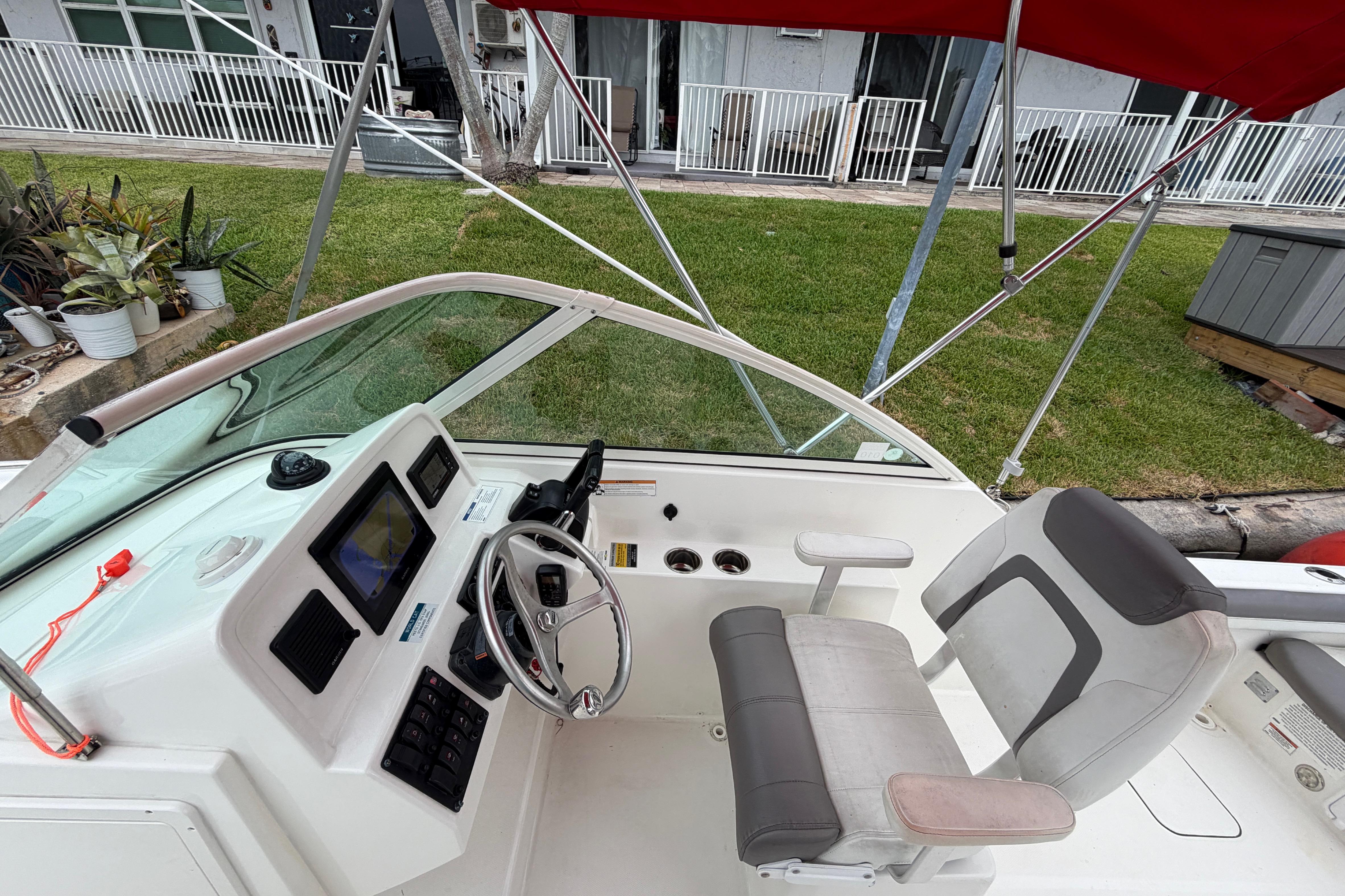 2019 World Cat 230 DC boat cockpit with steering wheel, navigation system, and seating under red canopy.