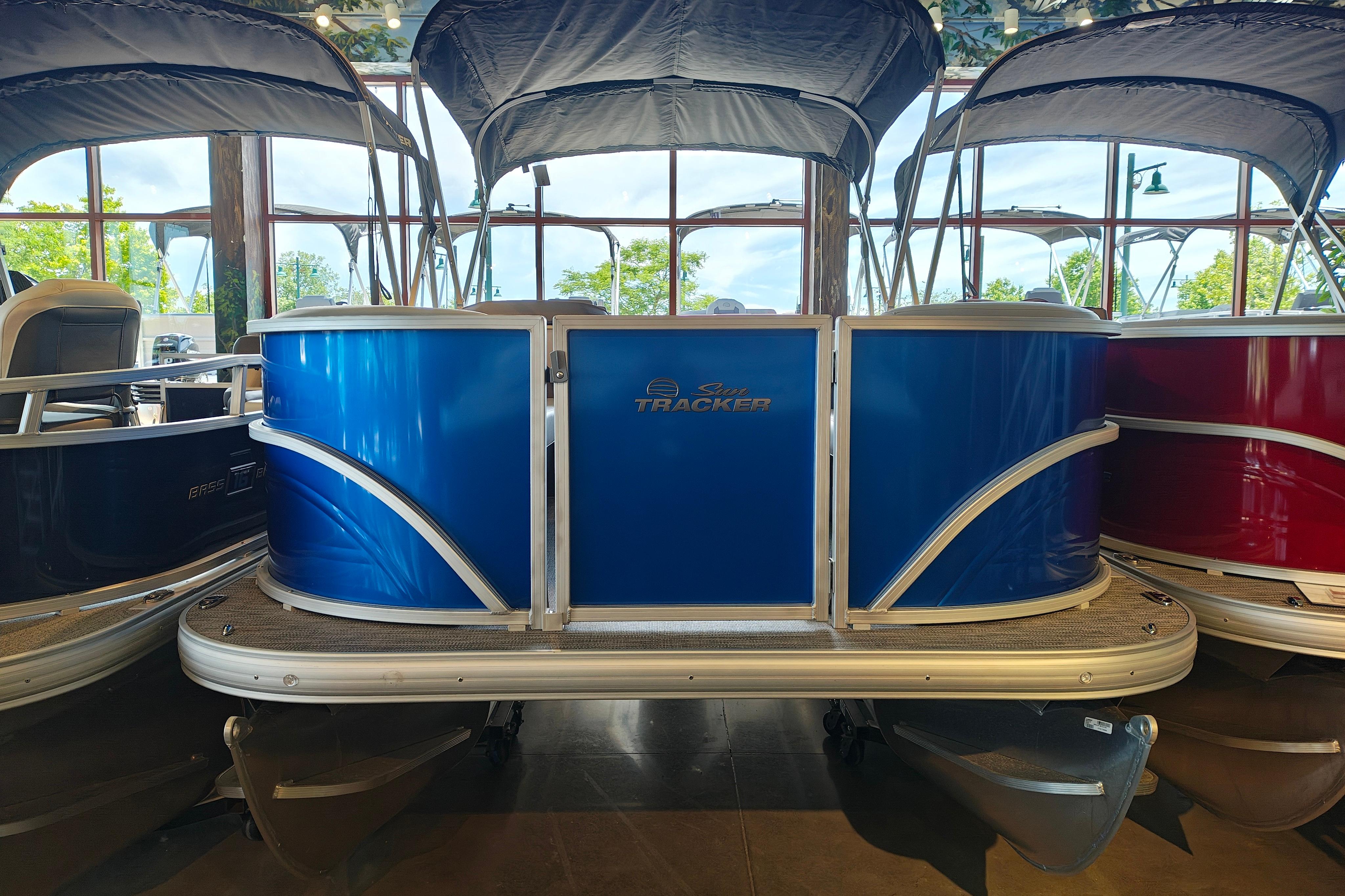 2026 Sun Tracker Party Barge 18 DLX pontoon boat in showroom, featuring blue exterior.