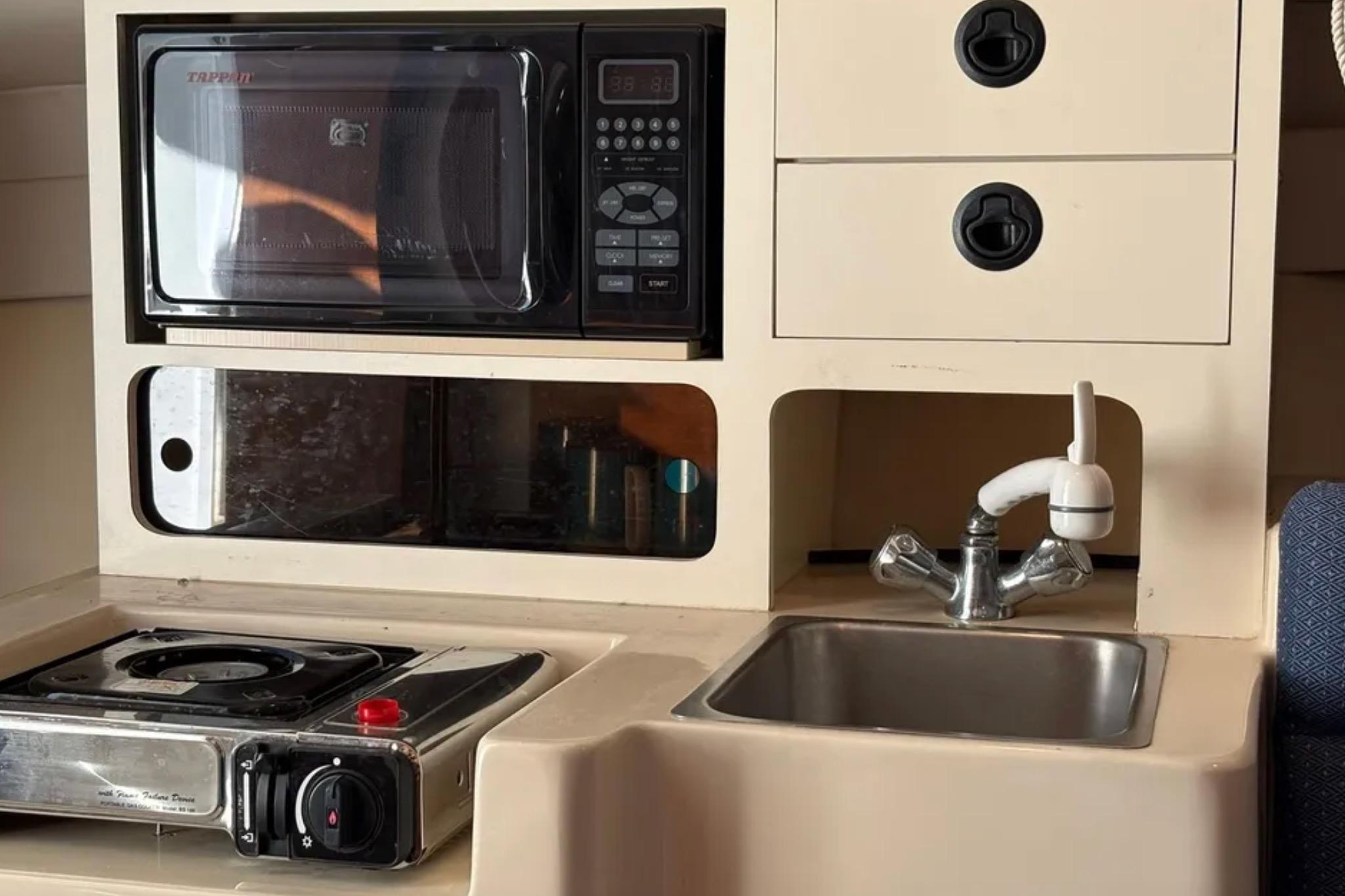 Compact kitchen area in a 2005 Albin 28 Tournament Express boat with stove, microwave, and sink.