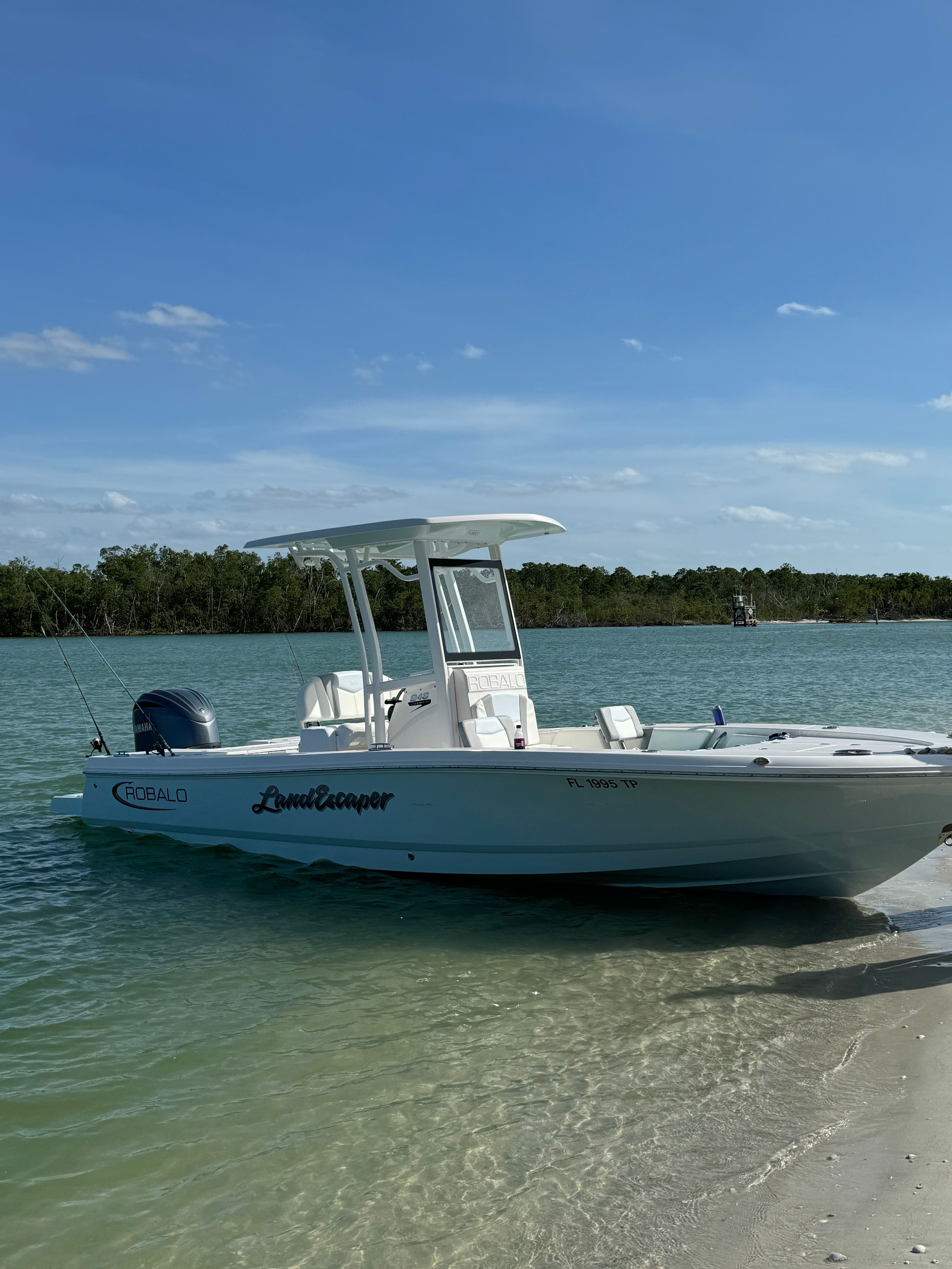 A white boat is beached on a calm water shore, with a clear sky in the background.